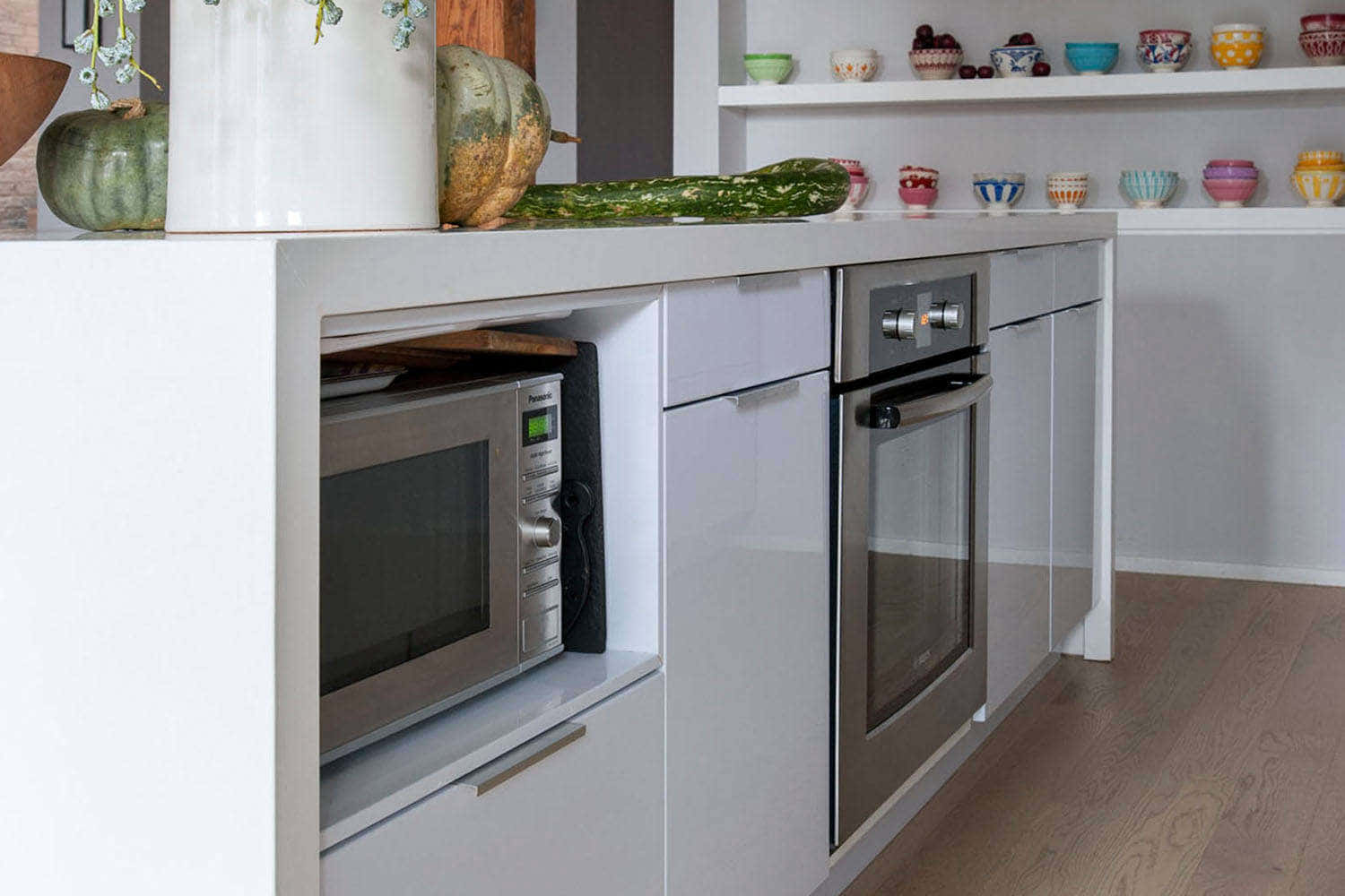 Microwave 桌布 壁紙 — 現代白色廚房島，內置微波爐和烤箱，周圍環繞著彩色陶瓷碗和秋季葫蘆。