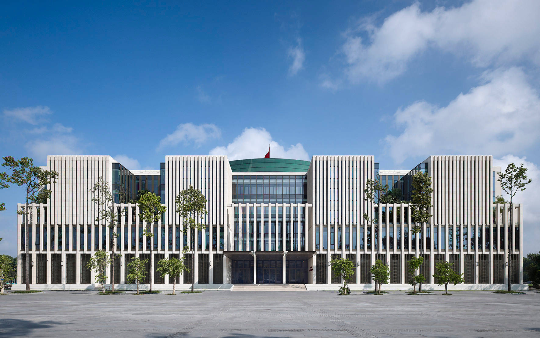Hanoi 桌布 壁紙 — 現代白色建築，帶有垂直條紋和玻璃幕牆，在明亮的藍天下有零星雲朵。