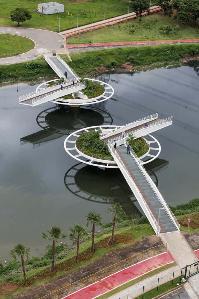 bridge 桌布 壁紙 — 現代白色螺旋橋橫跨平靜河流的鳥瞰圖，人們在散步，棕櫚樹排列在兩岸。