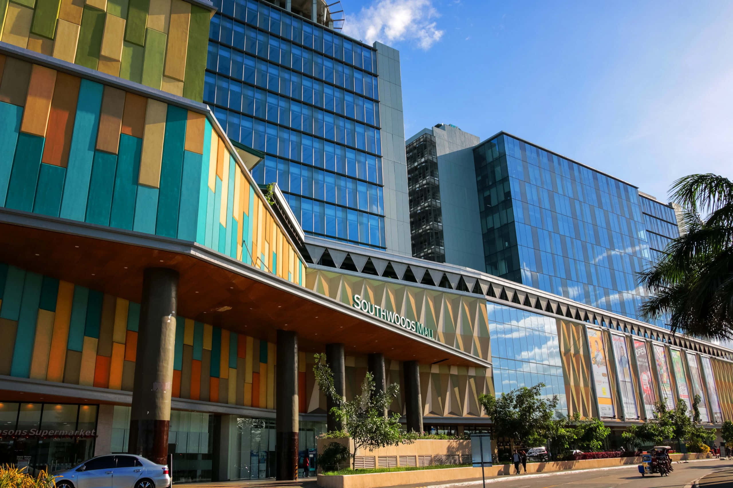 Mall 桌布 壁紙 — 現代的Southwoods Mall在晴朗藍天、棕櫚樹和汽車附近，展現出充滿活力的彩色面板和玻璃外牆。