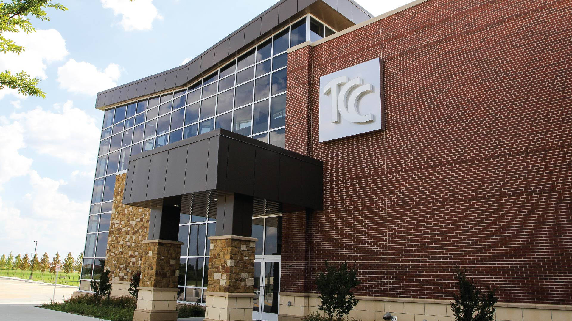 Oklahoma 桌布 壁紙 — 現代磚砌建築，玻璃外牆，帶有「TC」標誌，在明亮的藍天白雲下。