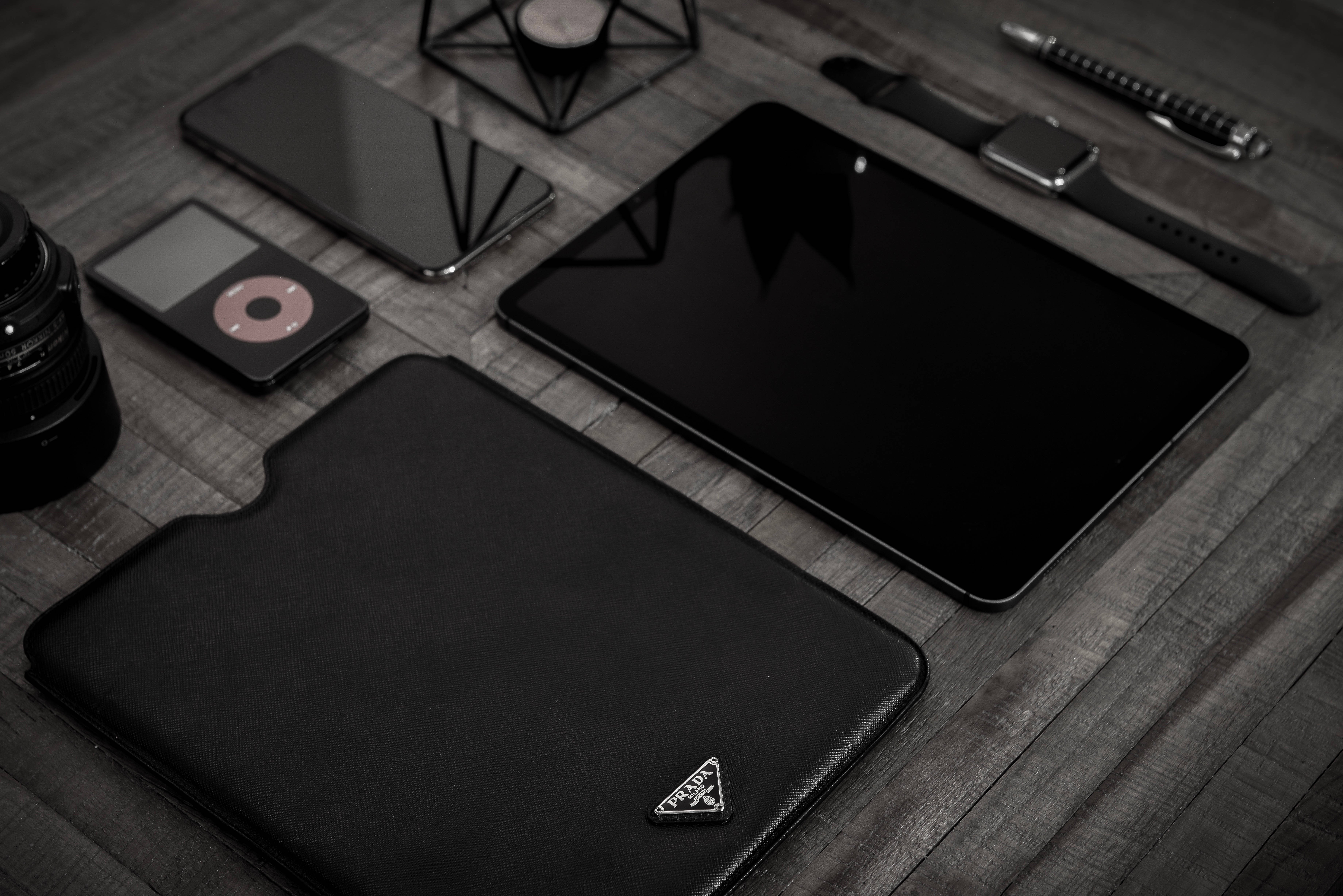 black apple iPhone 桌布 壁紙 — 現代科技產品包括平板電腦、手機、手錶和相機整齊地排列在深色木質表面上。