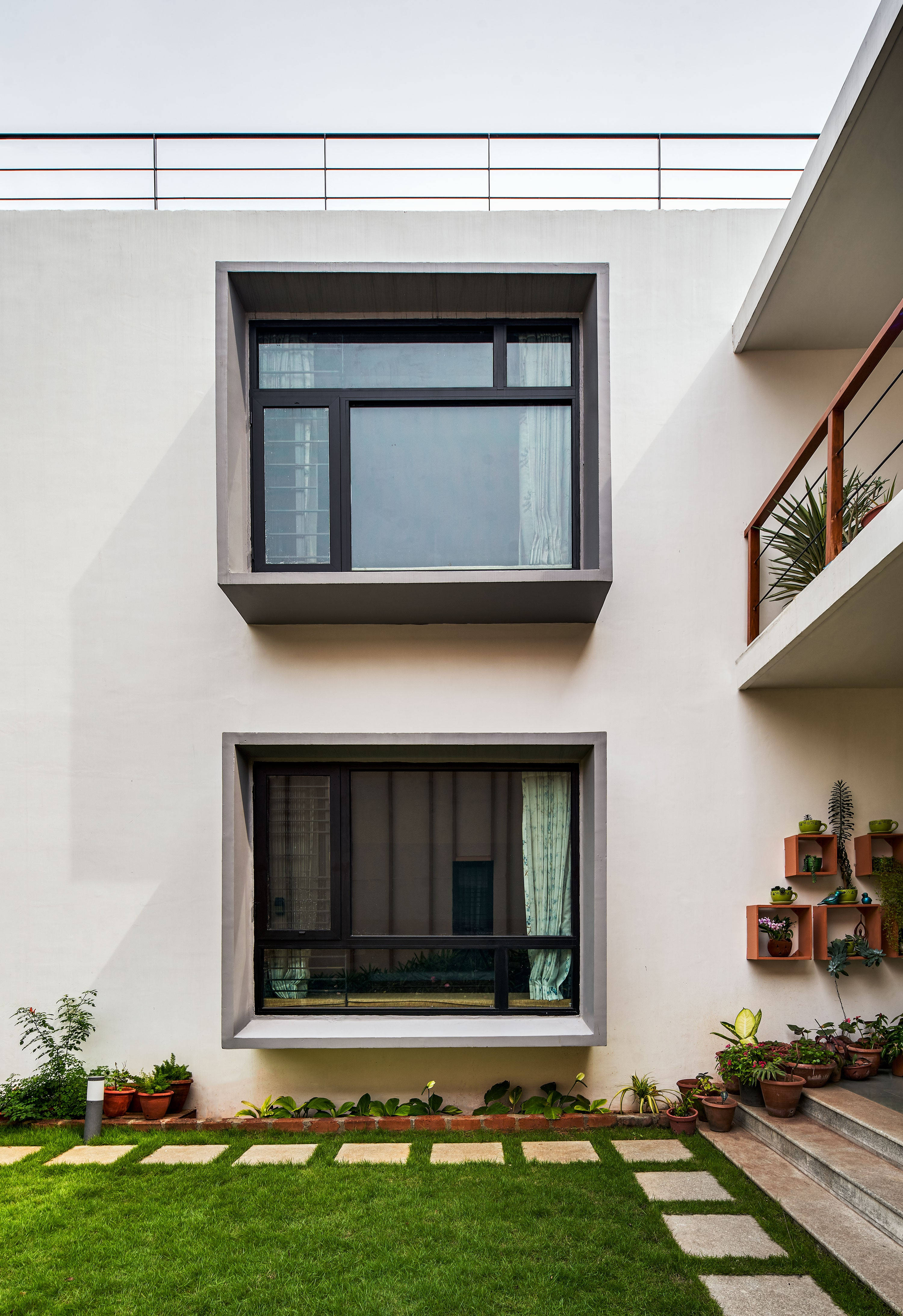 Home 桌布 壁紙 — 現代簡約庭院，白色牆壁，兩扇大窗，盆栽植物，石徑，明亮日光下。