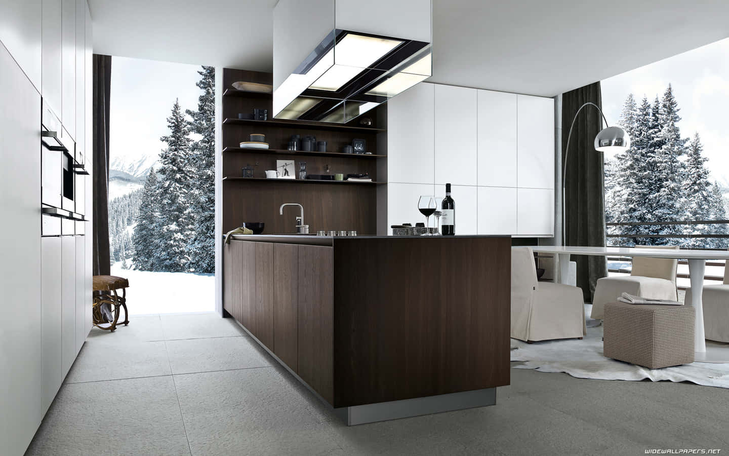 1440p Kitchen 桌布 壁紙 — 現代簡約廚房，設有深色木質中島和白色櫥櫃，透過大窗戶俯瞰白雪覆蓋的松樹林。