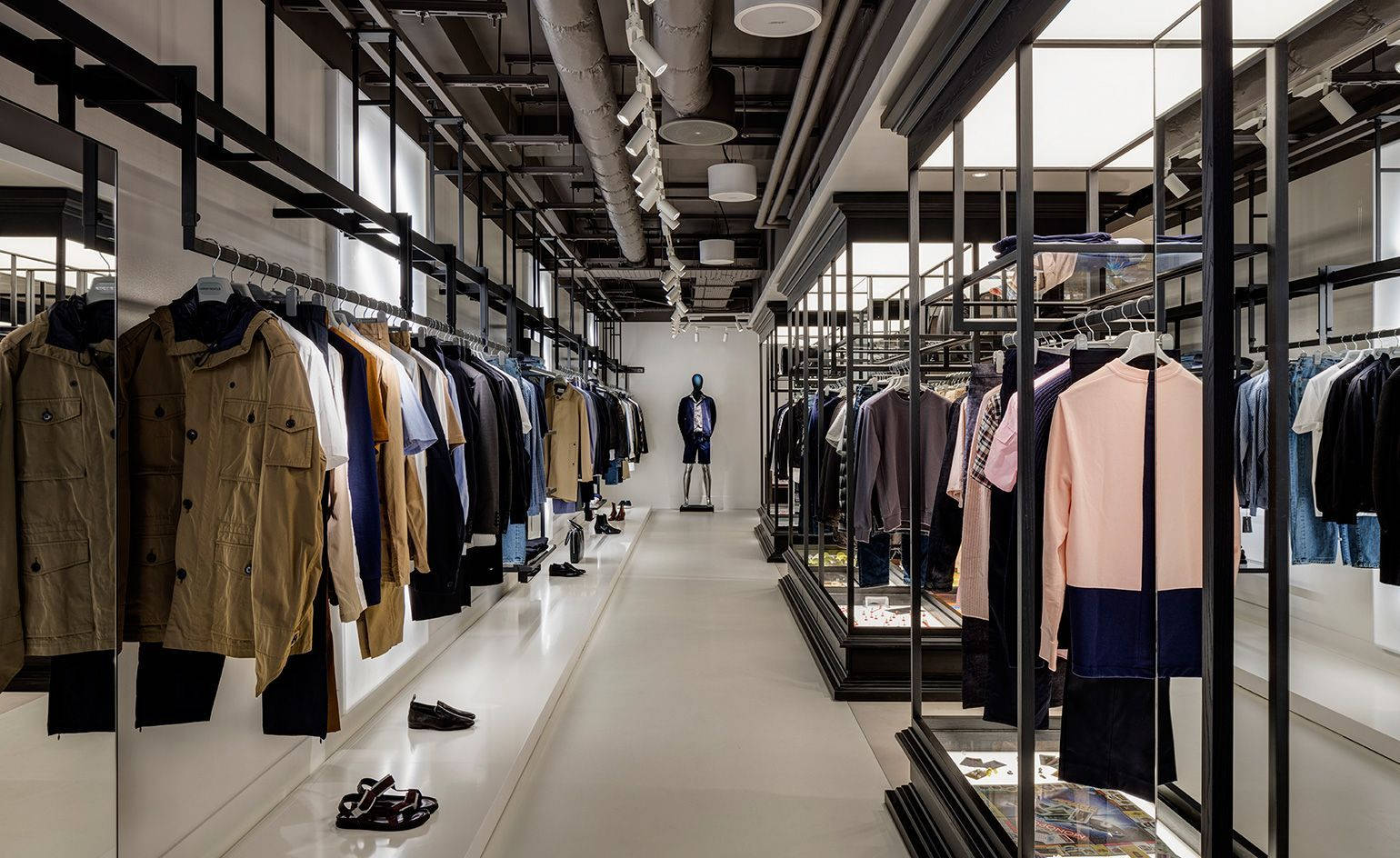 Clothes 桌布 壁紙 — 現代簡約服裝店，配有時尚黑色貨架、白色牆壁，以及工業風天花板燈光下的中央人體模型。
