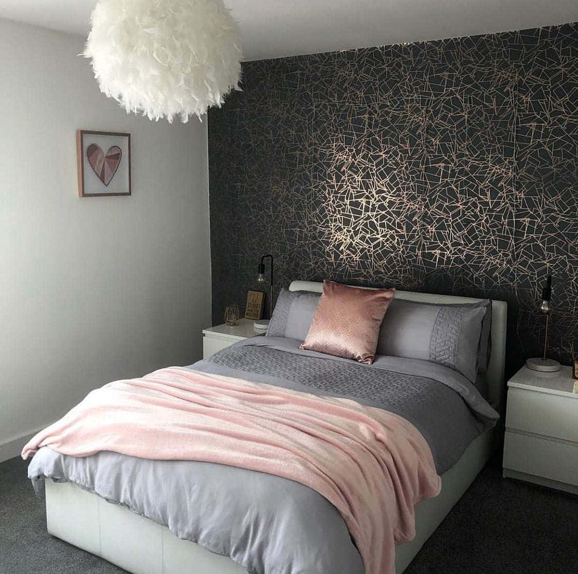 bed 桌布 壁紙 — 現代臥室配有一張灰色床單和粉色毯子的床，下方是蓬鬆的白色吊燈，背景是深色幾何壁紙。