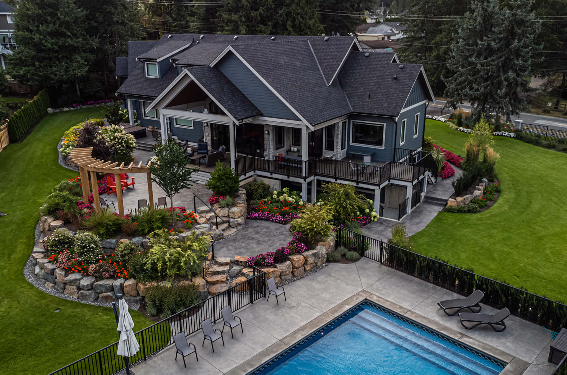 Luxury House 桌布 壁紙 — 現代藍色房屋的鳥瞰圖，設有游泳池和充滿活力的花園，周圍環繞著茂密的綠色草坪和高大的樹木。