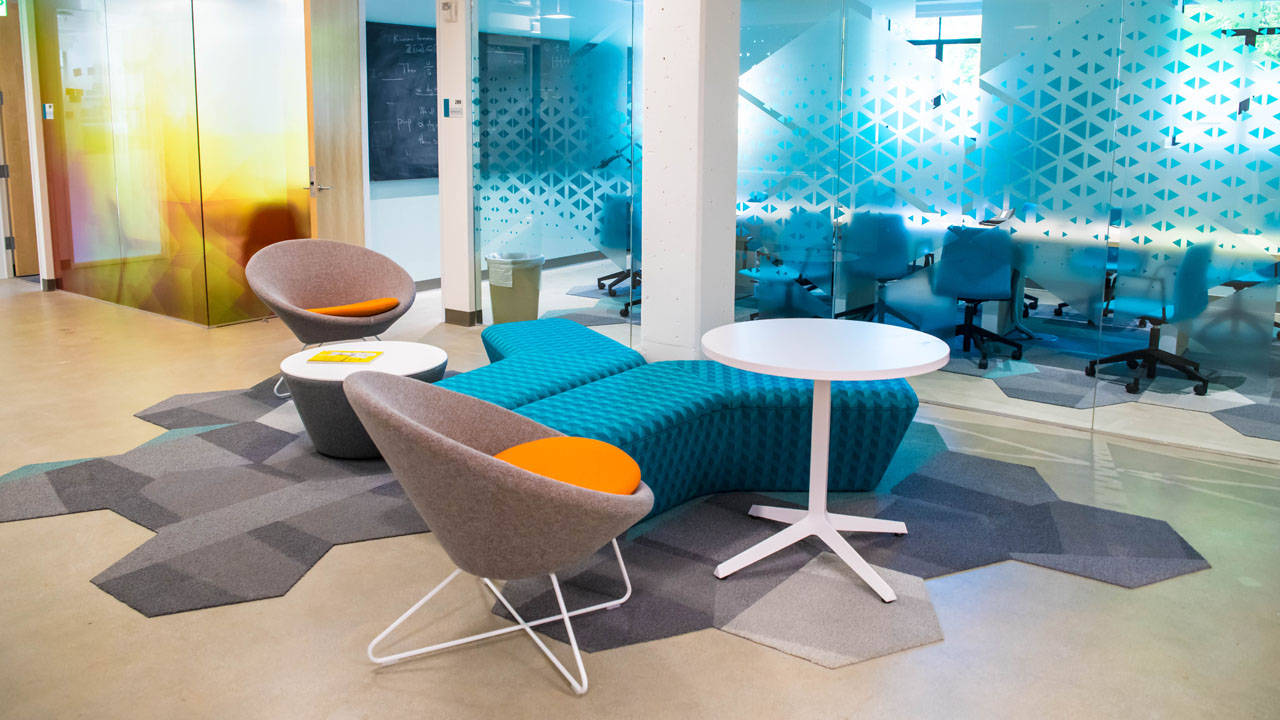 Interior Design 桌布 壁紙 — 現代辦公室休息區，配有青綠色模組化沙發、橙色靠墊、幾何圖案地毯和反射藍色椅子的玻璃隔斷。