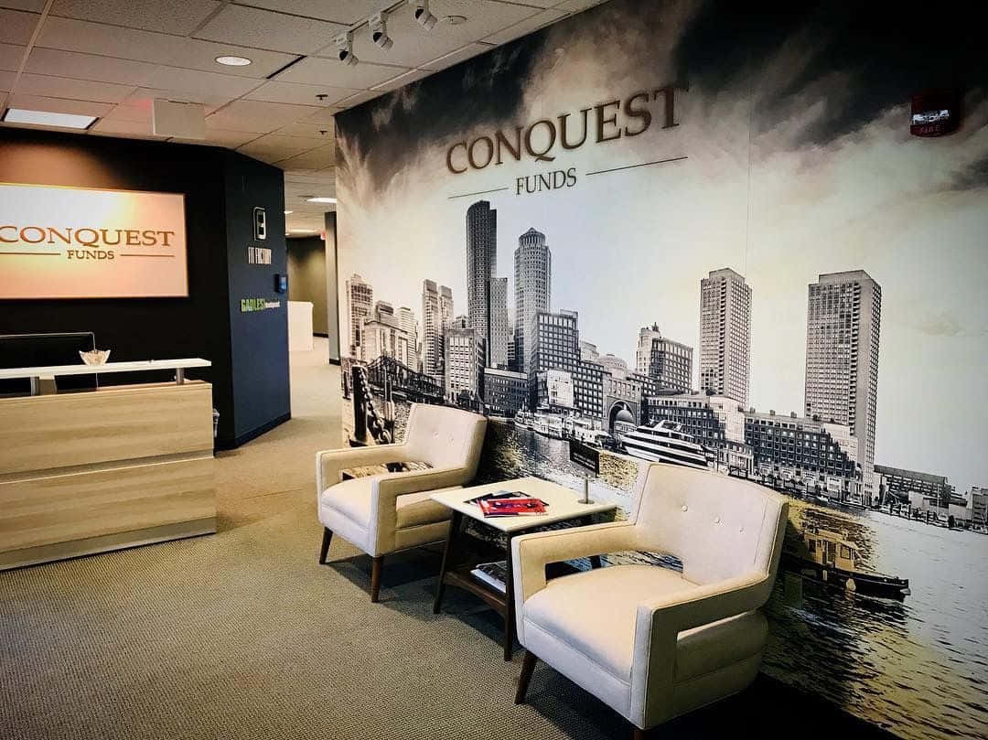 辦公室 桌布 壁紙 — 現代辦公室大廳，配有奶油色椅子，面向一幅標有 Conquest Funds 的大型黑白城市景觀壁畫。