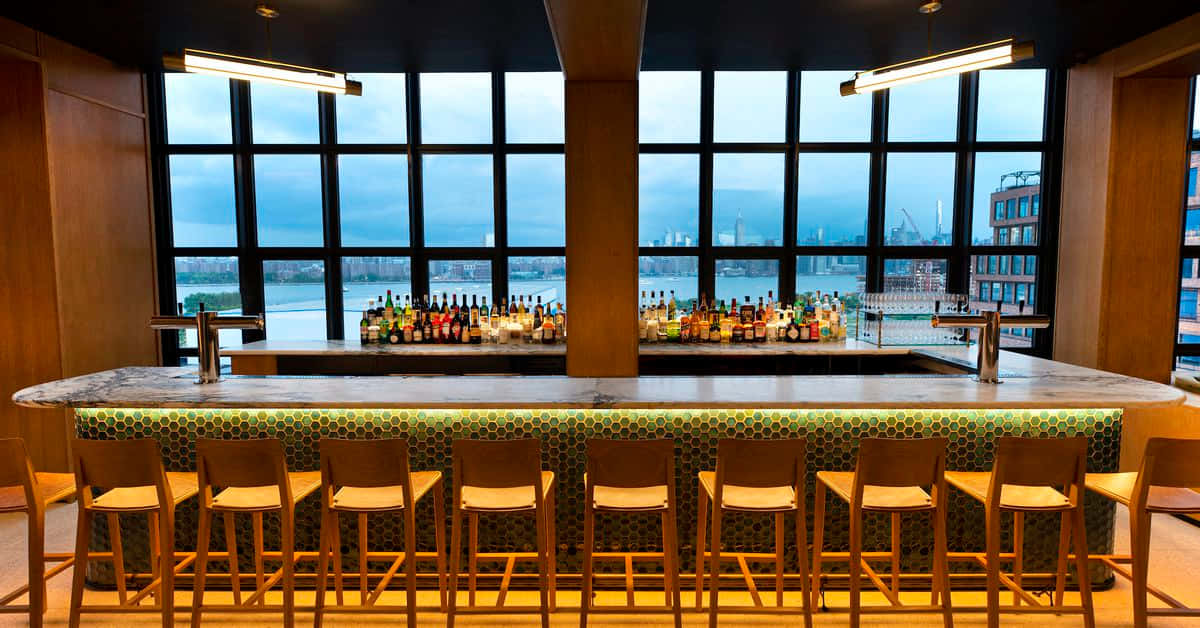 Bar 桌布 壁紙 — 現代酒吧，配有木凳和蜂巢瓷磚防濺板，透過大窗戶俯瞰海濱城市景觀。