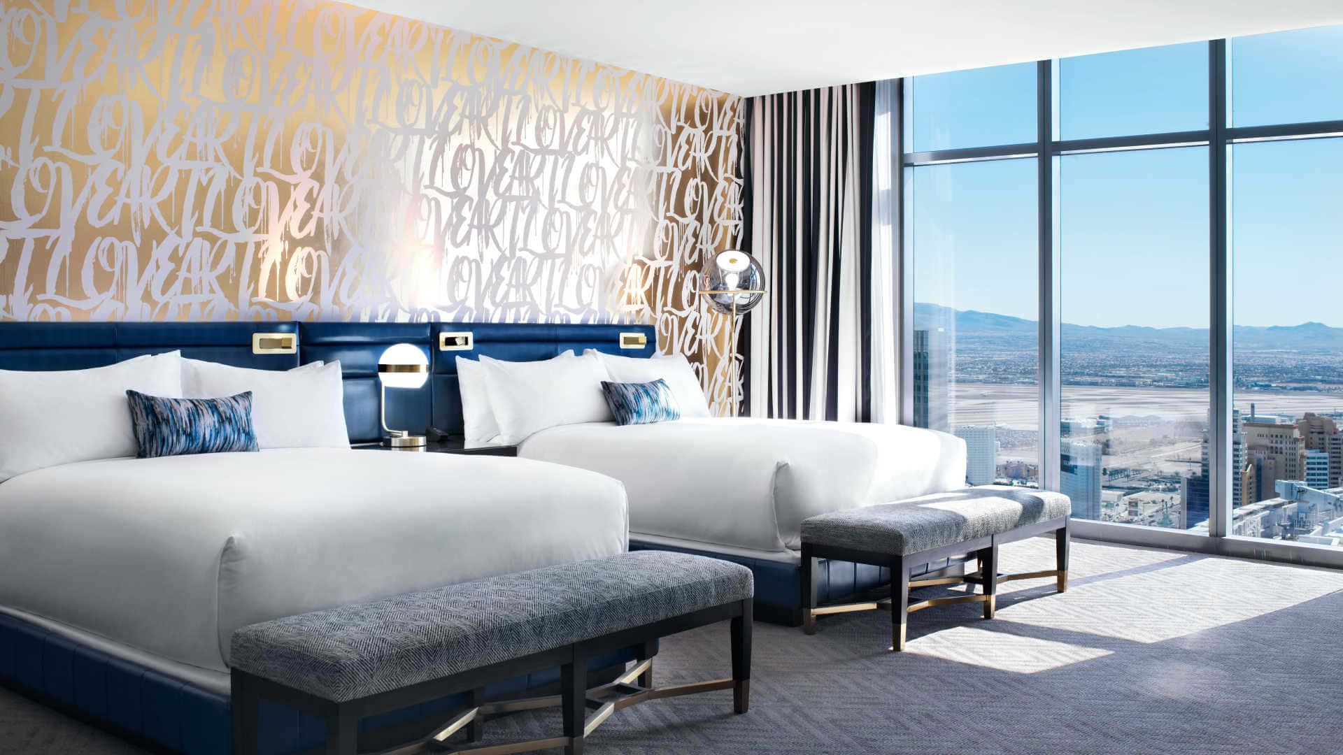 Hotel Room 桌布 壁紙 — 現代酒店客房，配備兩張床和一幅大膽的愛情主題壁紙，透過落地窗可欣賞城市景觀。