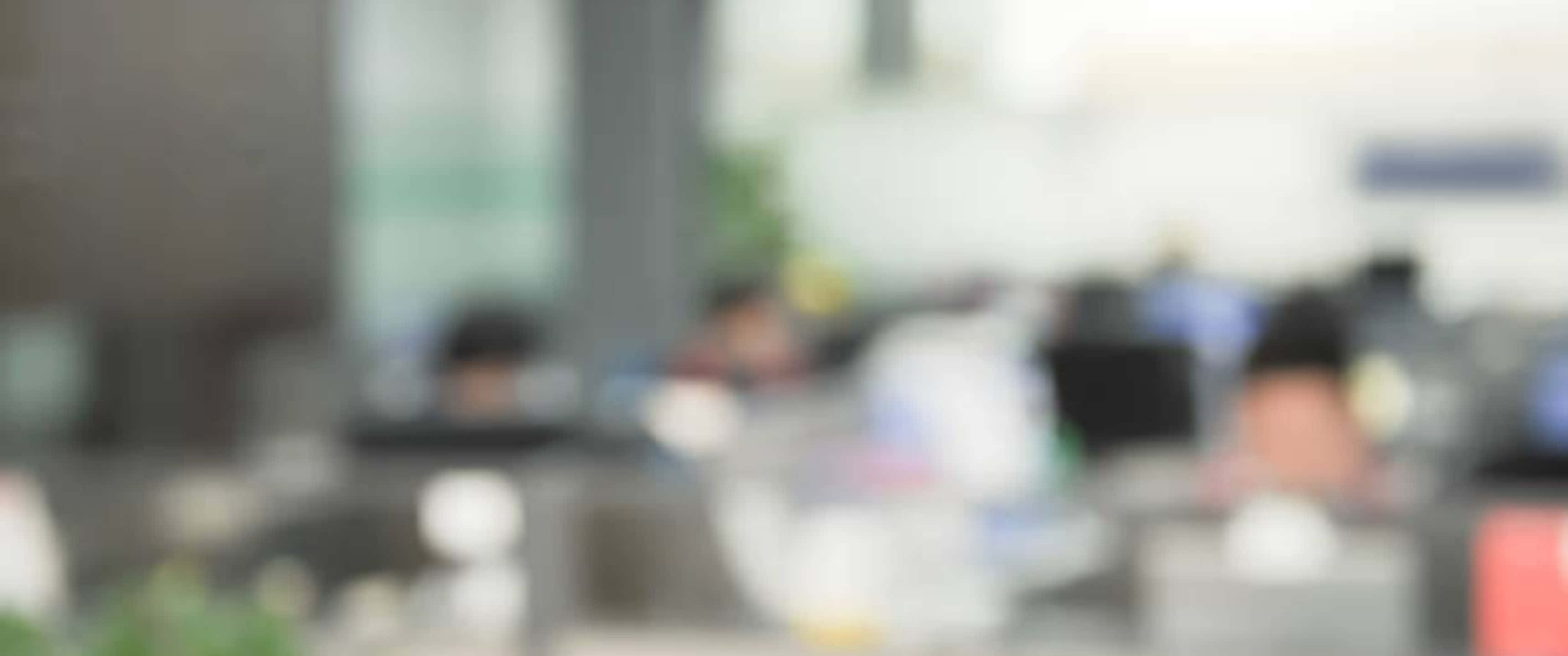 Blurred Office 桌布 壁紙 — 現代開放式工作空間中，辦公桌旁模糊的辦公室員工，柔和自然光線。