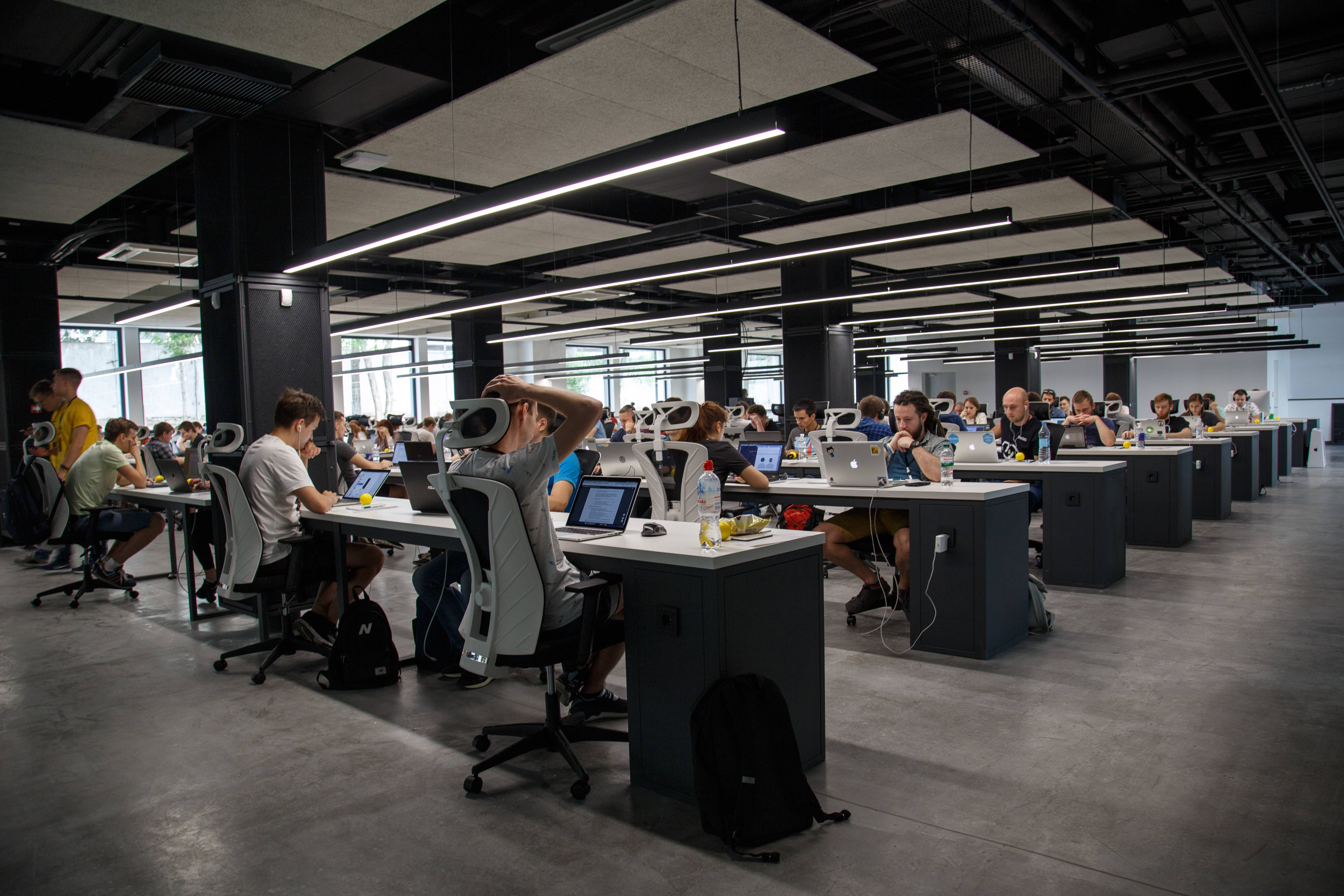 Office 桌布 壁紙 — 現代開放式辦公室，一排排員工在明亮的頭頂燈光下專注於筆記型電腦。