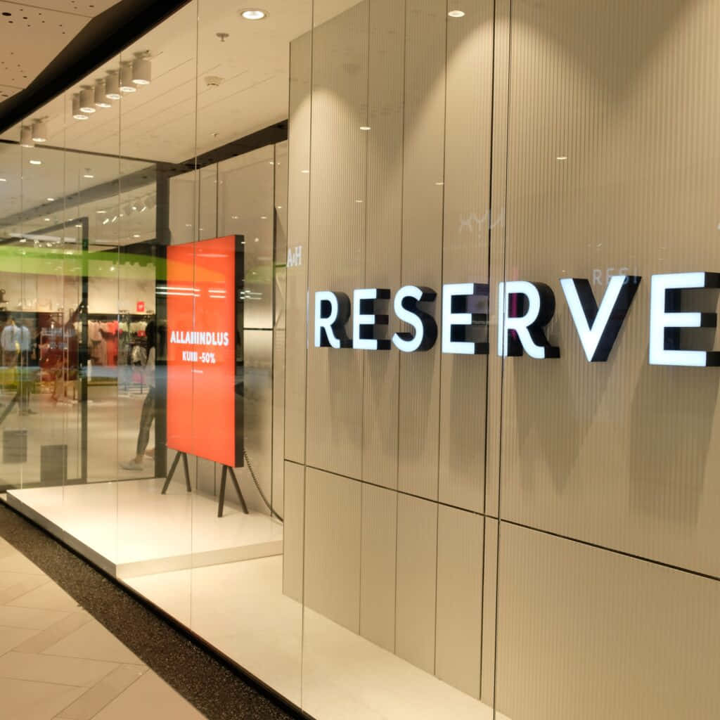 高清 桌布 壁紙 — 現代零售店面，帶有發光的「RESERVE」標誌和橙色促銷海報，透過玻璃窗可見。