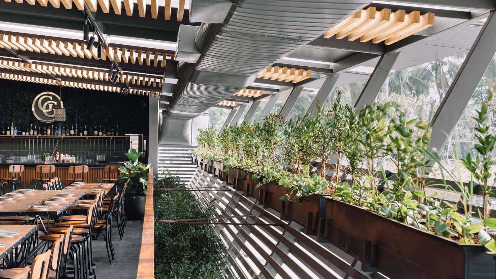 Interior 桌布 壁紙 — 現代餐廳內部，設有木製桌椅，陽光透過玻璃牆，牆邊種滿茂盛的綠色植物。