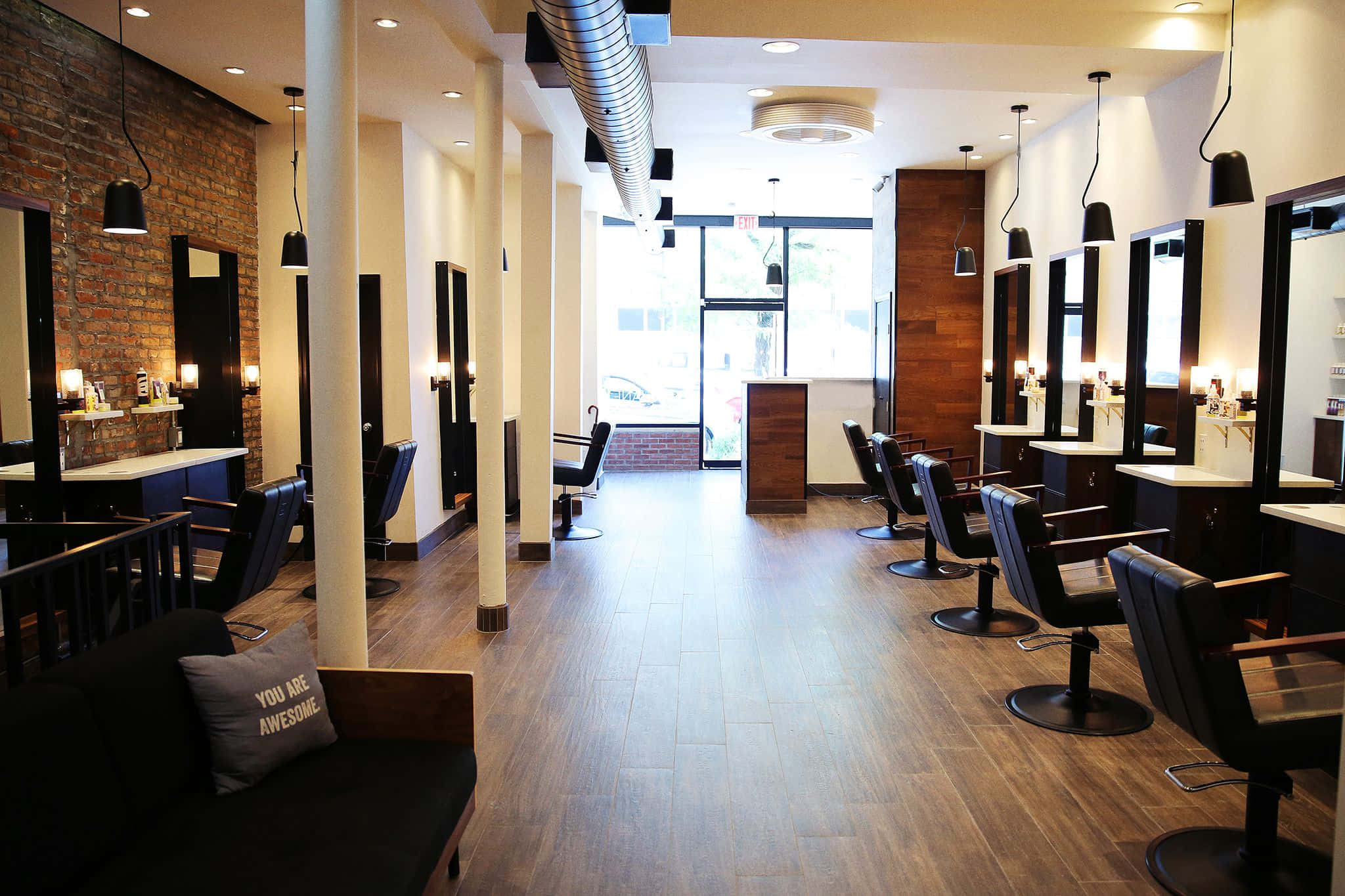 Hair Salon 桌布 壁紙 — 現代髮廊，設有黑色椅子、鏡子、裸露磚牆和溫暖燈光，沿著木地板走廊。