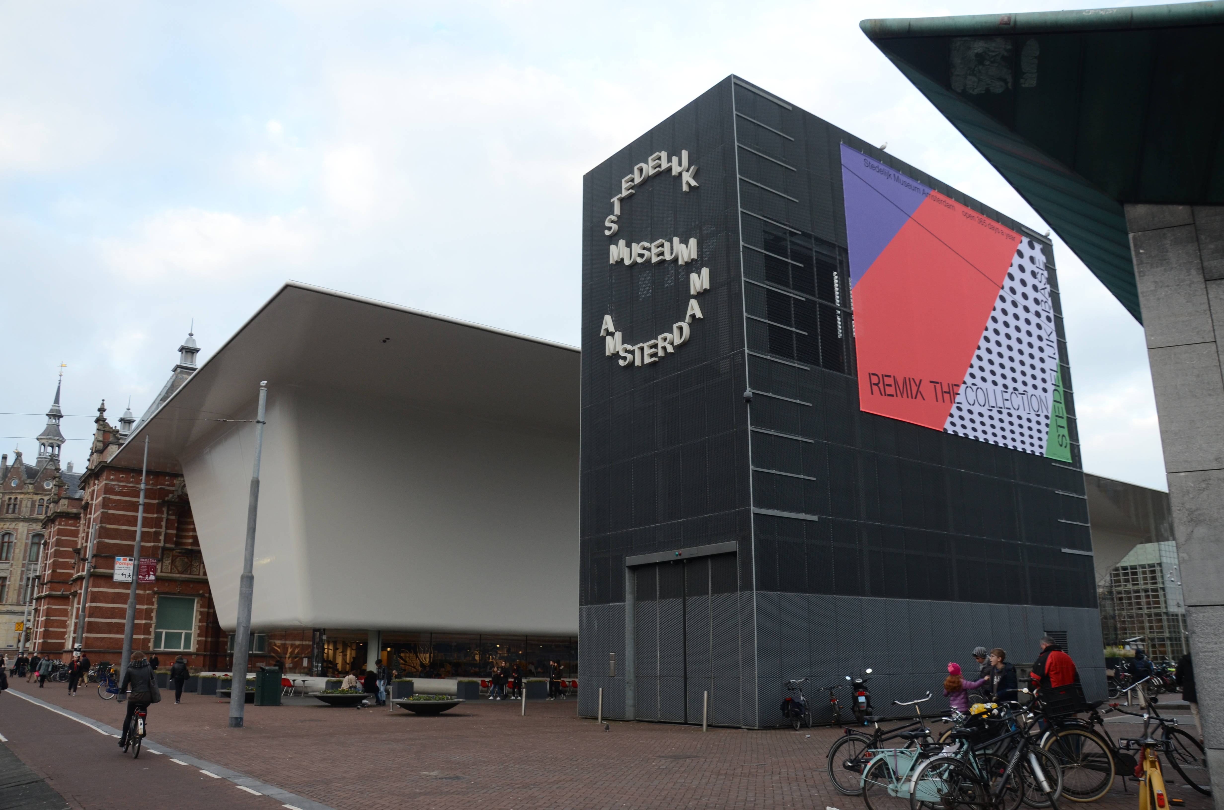 Amsterdam 桌布 壁紙 — 現代黑白博物館建築，帶有色彩繽紛的幾何壁畫，矗立在歷史悠久的紅磚建築旁，天空多雲。