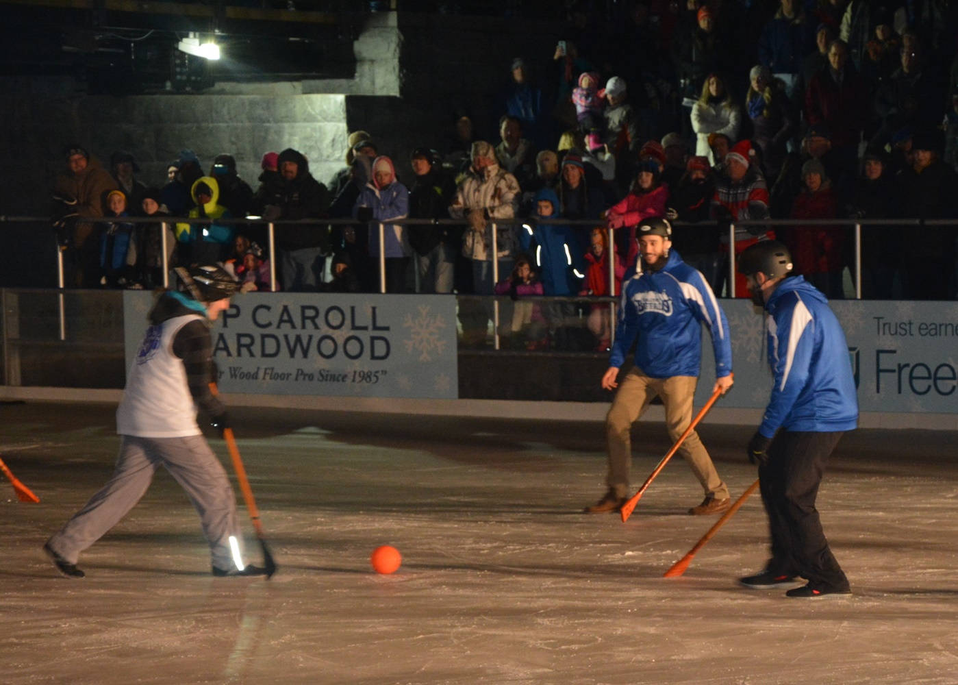 運動 桌布 壁紙 — 球員在明亮的燈光下於溜冰場上進行冰上 broomball 比賽，觀眾從看台觀看。