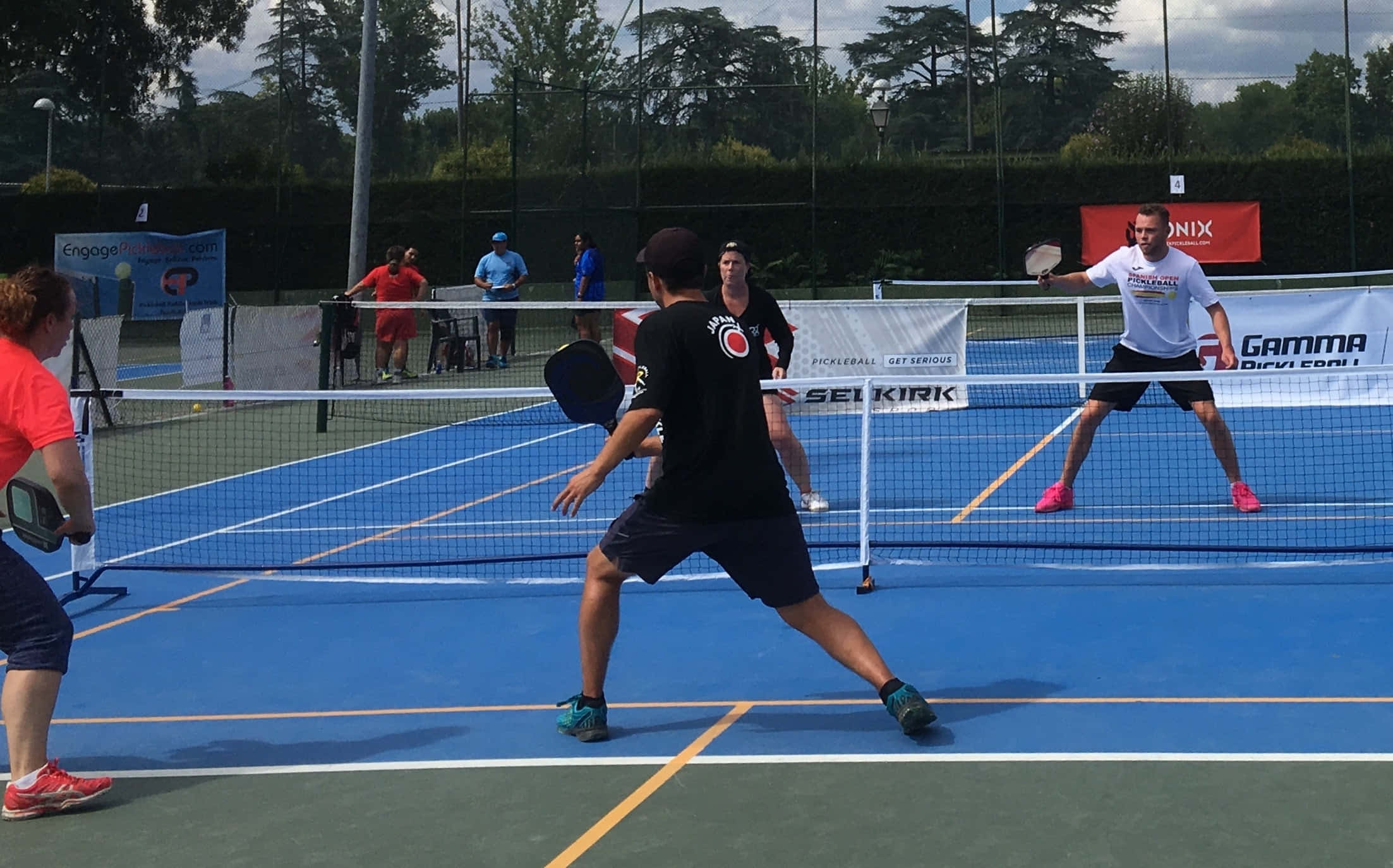 Pickleball 桌布 壁紙 — 球員在陰天下的明亮藍色球場上激烈地進行匹克球比賽。