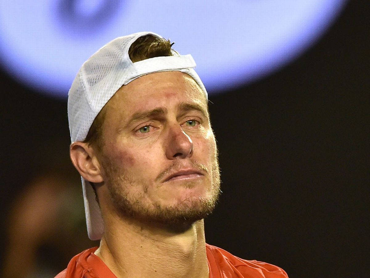 Australian Open 桌布 壁紙 — 球場燈光下，一名疲憊的男性網球運動員戴著白色帽子、穿著橙色襯衫的特寫。