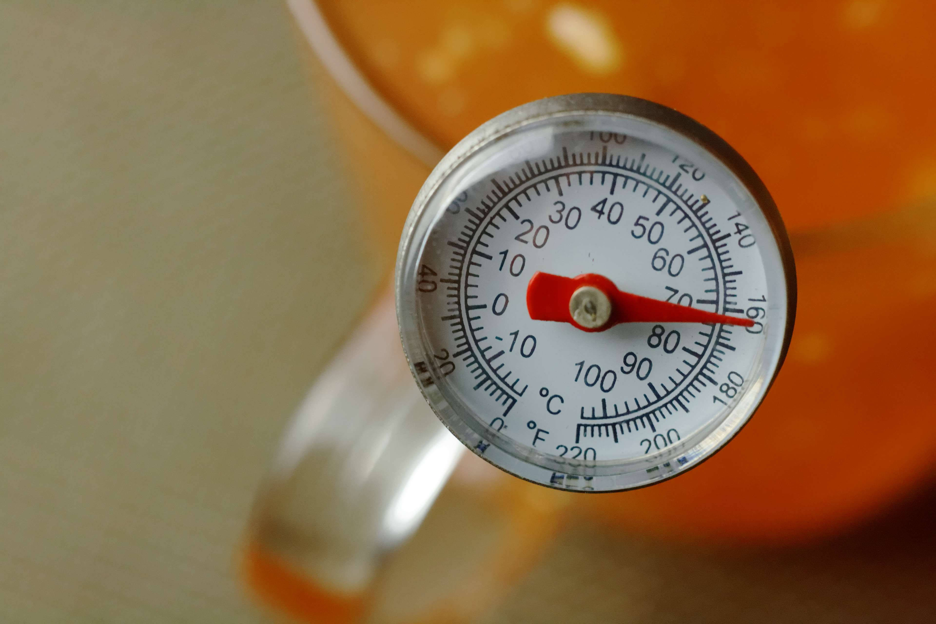 Temperature 桌布 壁紙 — 琥珀色液體玻璃杯中的紅色針式溫度計特寫，顯示攝氏和華氏溫度。