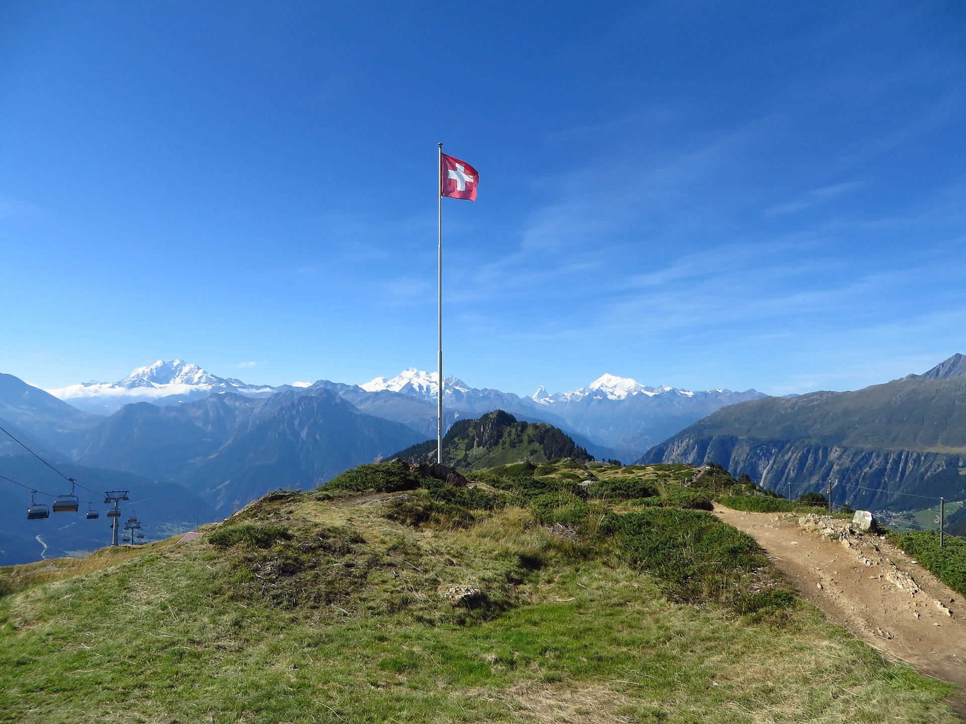 Alps 桌布 壁紙 — 瑞士國旗在一個長滿草的山脊上飄揚，背景是白雪覆蓋的山峰和晴朗的藍天。