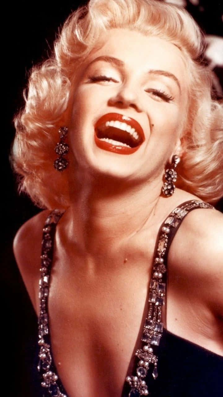 Marilyn Monroe iPhone 桌布 壁紙 — 瑪麗蓮夢露在深色背景前，帶著鮮紅的嘴唇和閃閃發光的珠寶，開懷大笑。