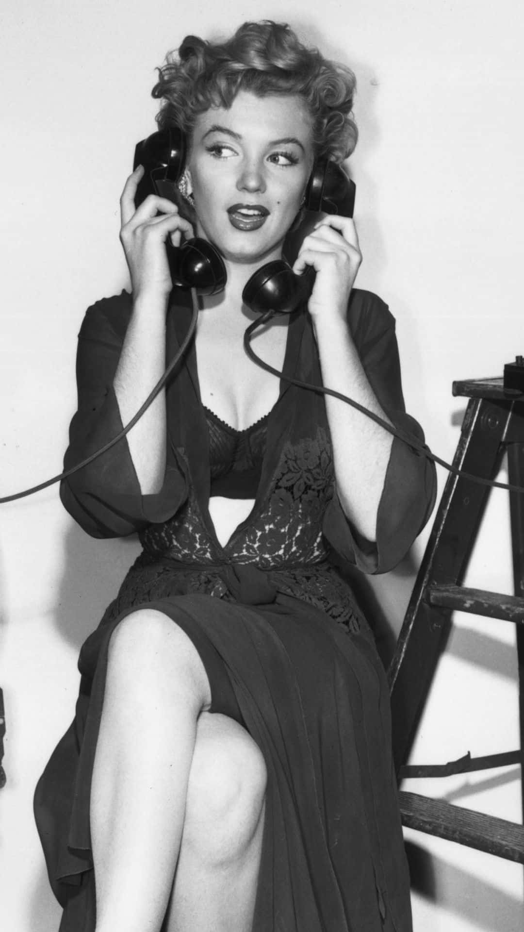 Marilyn Monroe iPhone 桌布 壁紙 — 瑪麗蓮夢露在經典黑白工作室肖像中，俏皮地將兩部復古電話聽筒貼在耳朵上。