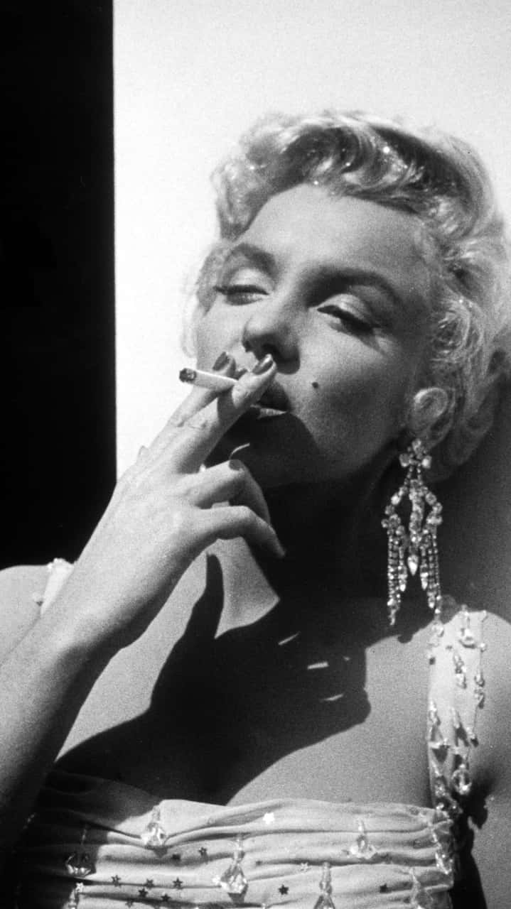 Marilyn Monroe iPhone 桌布 壁紙 — 瑪麗蓮夢露在迷人的黑白肖像中吸煙，配以戲劇性燈光和閃閃發光的珠寶。