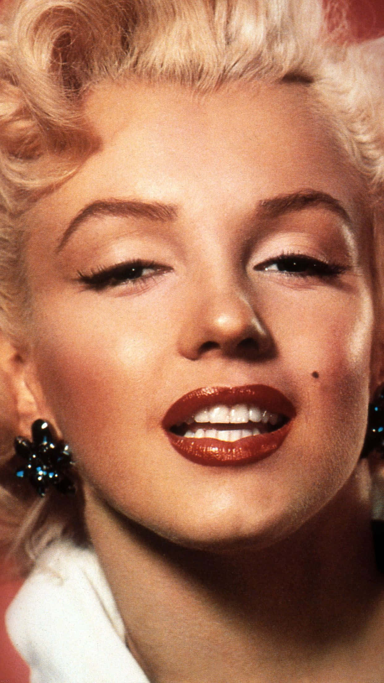 Marilyn Monroe iPhone 桌布 壁紙 — 瑪麗蓮夢露的特寫肖像，金色捲髮、紅唇和閃閃發光的耳環，對著鏡頭溫柔微笑。