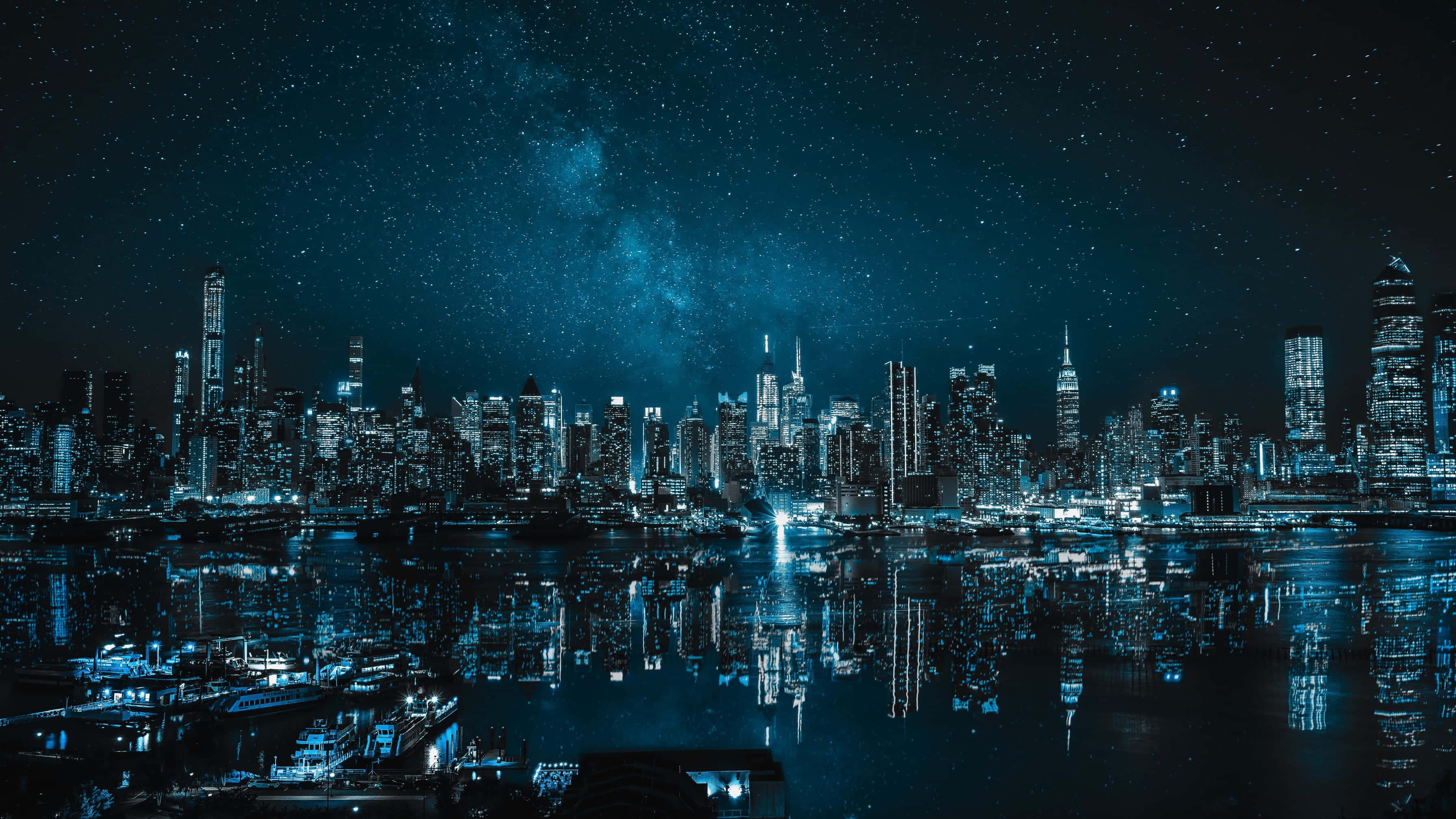 City Lights 桌布 壁紙 — 璀璨的夜景，摩天大樓在星空下倒映在水中，銀河清晰可見。