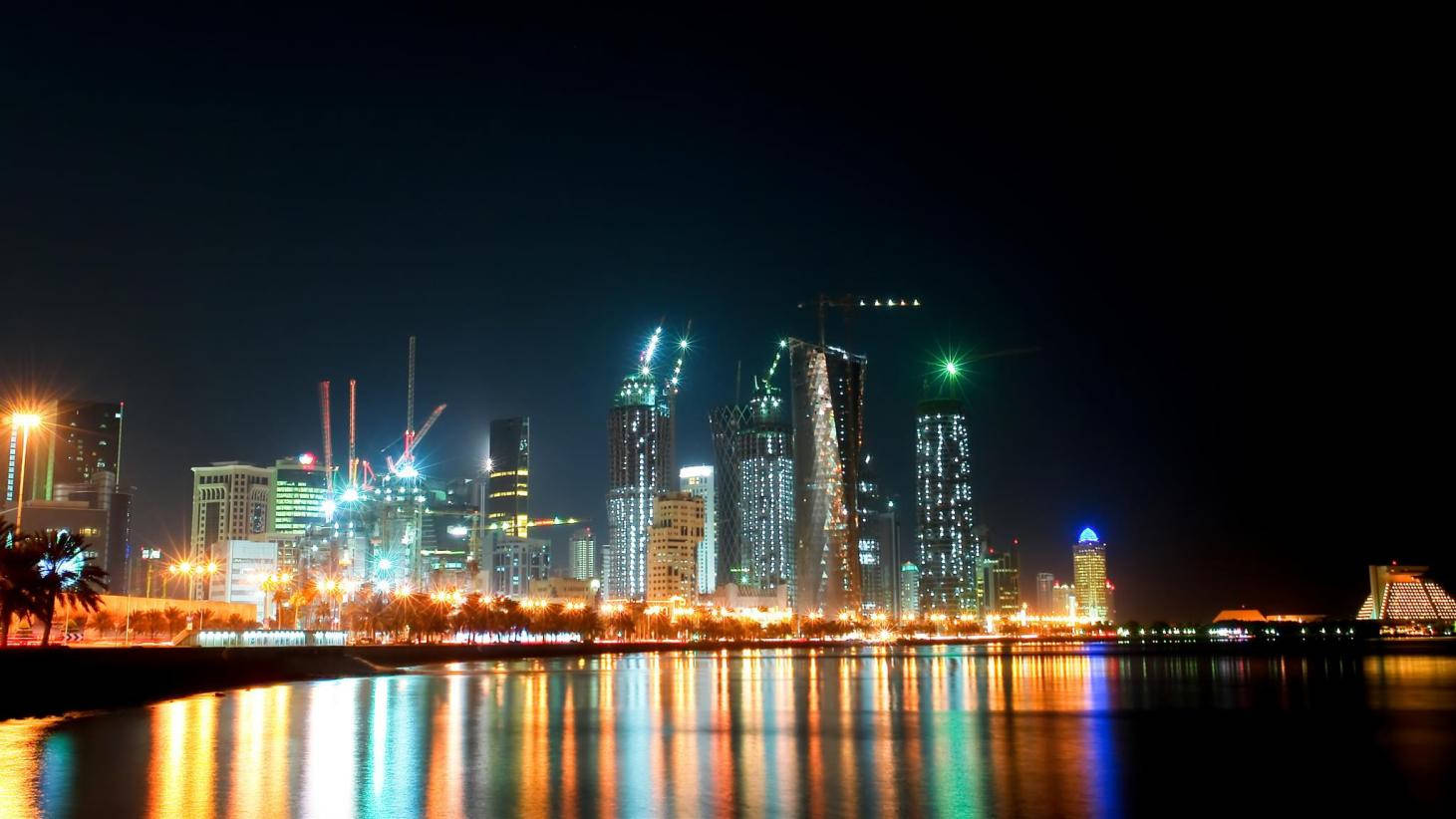 Qatar 桌布 壁紙 — 璀璨的夜景城市景觀，燈火通明的摩天大樓和建築起重機倒映在平靜的水面上。