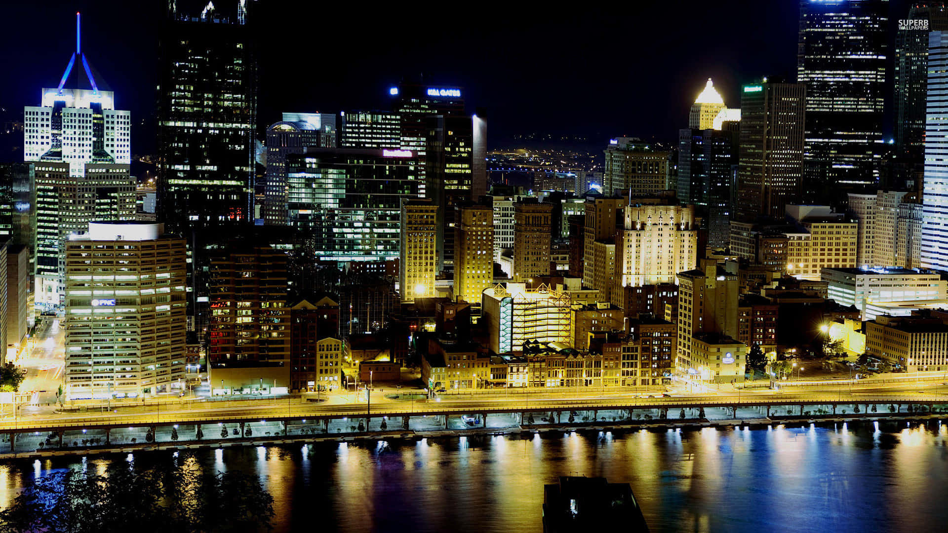 Pittsburgh Skyline 桌布 壁紙 — 璀璨的夜景城市景觀，燈火通明的摩天大樓倒映在下方漆黑的河流中。