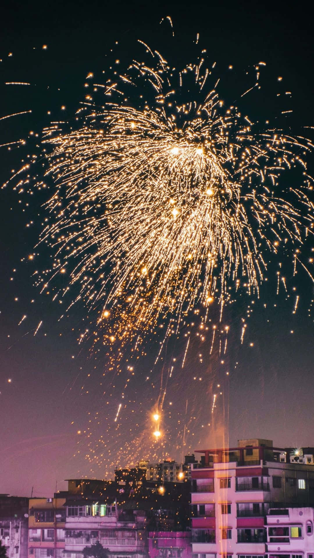 桌布 壁紙 — 璀璨的金色煙火在夜間的城市景觀上空爆炸，在黑暗的天空中灑下火花。