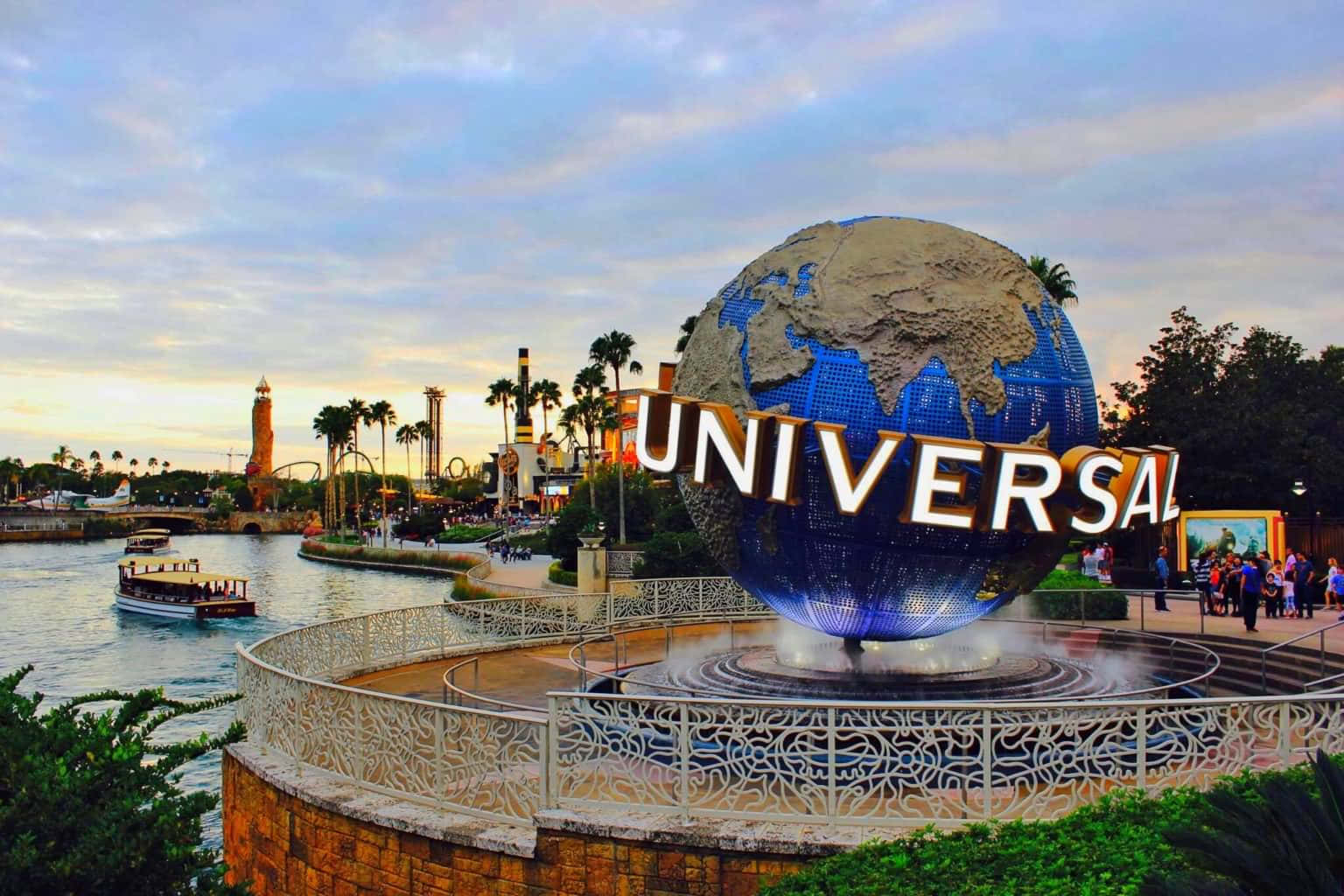 Universal 桌布 壁紙 — 環球影城標誌性的地球儀在黃昏時發光，一艘船在種滿棕櫚樹和主題公園景點的運河上行駛。