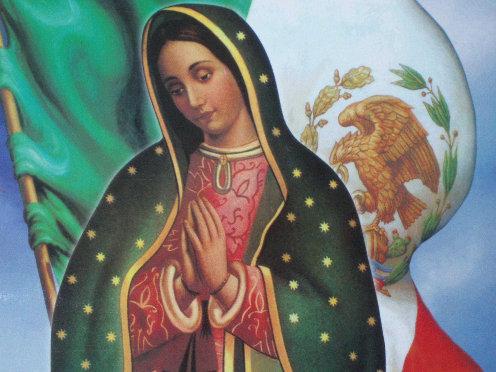 Mexican 桌布 壁紙 — 瓜達露佩聖母身穿傳統服飾，雙手合十，站在帶有鷹和仙人掌的墨西哥國旗前。