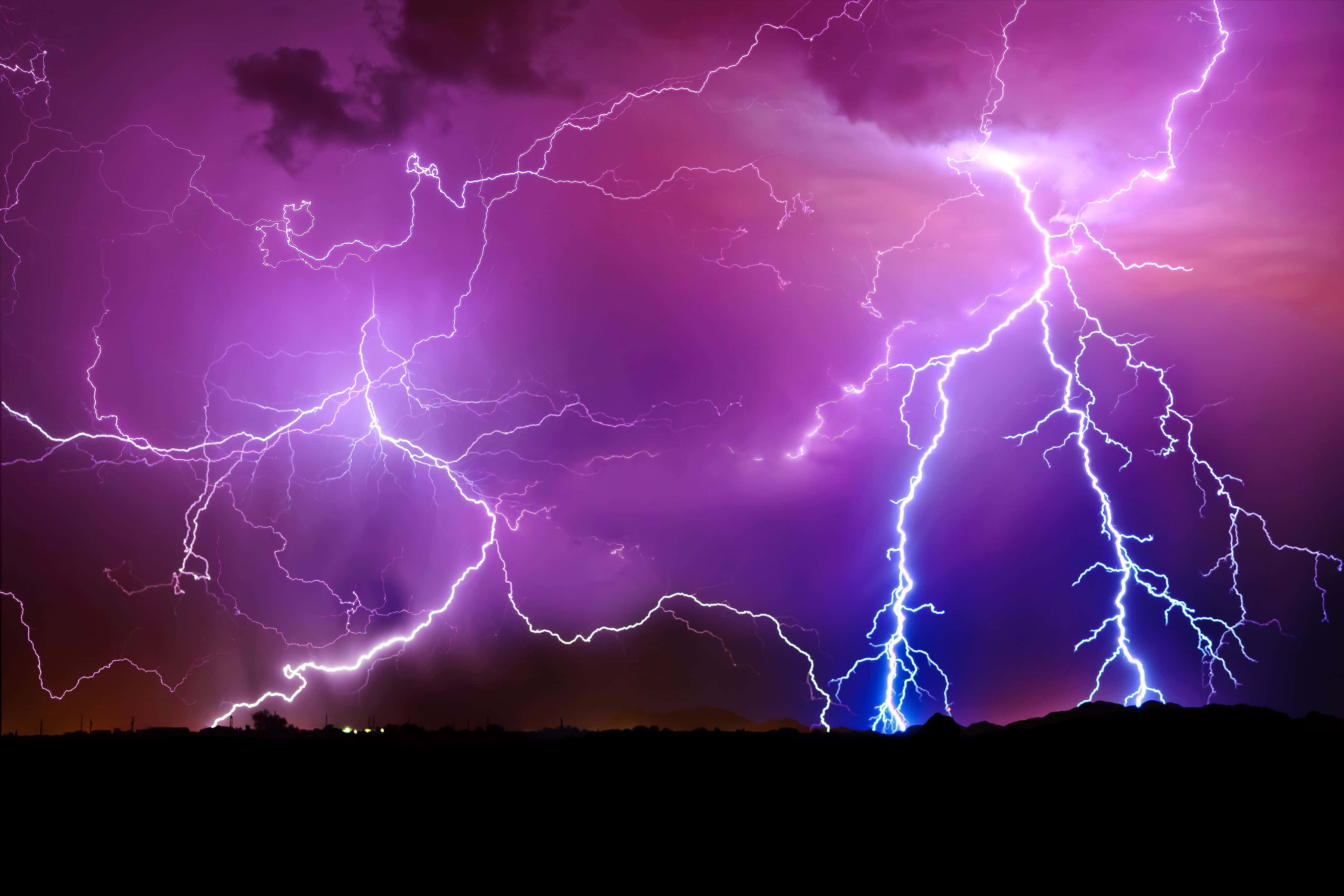 閃電 桌布 壁紙 — 生動的紫色和藍色閃電在暴風雨的夜空中劈啪作響，掠過黑暗的山丘輪廓。