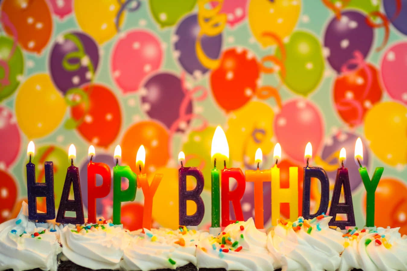 Birthday Celebration 桌布 壁紙 — 生日蛋糕特寫，上面有彩色字母蠟燭拼出 'HAPPY BIRTHDAY'，背景是充滿活力的氣球圖案。