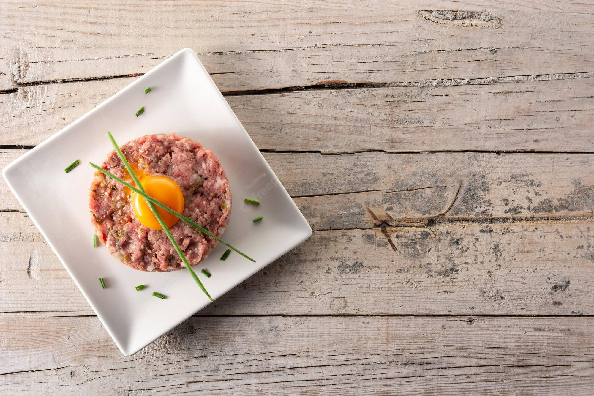 meat 桌布 壁紙 — 生牛肉他他，上面放著鮮黃色的蛋黃和新鮮細香蔥，放在白色方形盤中，置於經風化的木板上。