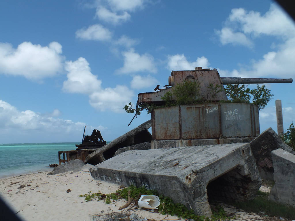 Kiribati 桌布 壁紙 — 生鏽廢棄的軍事碉堡，長滿茂密植被，矗立在沙灘上，天空湛藍，白雲點點。