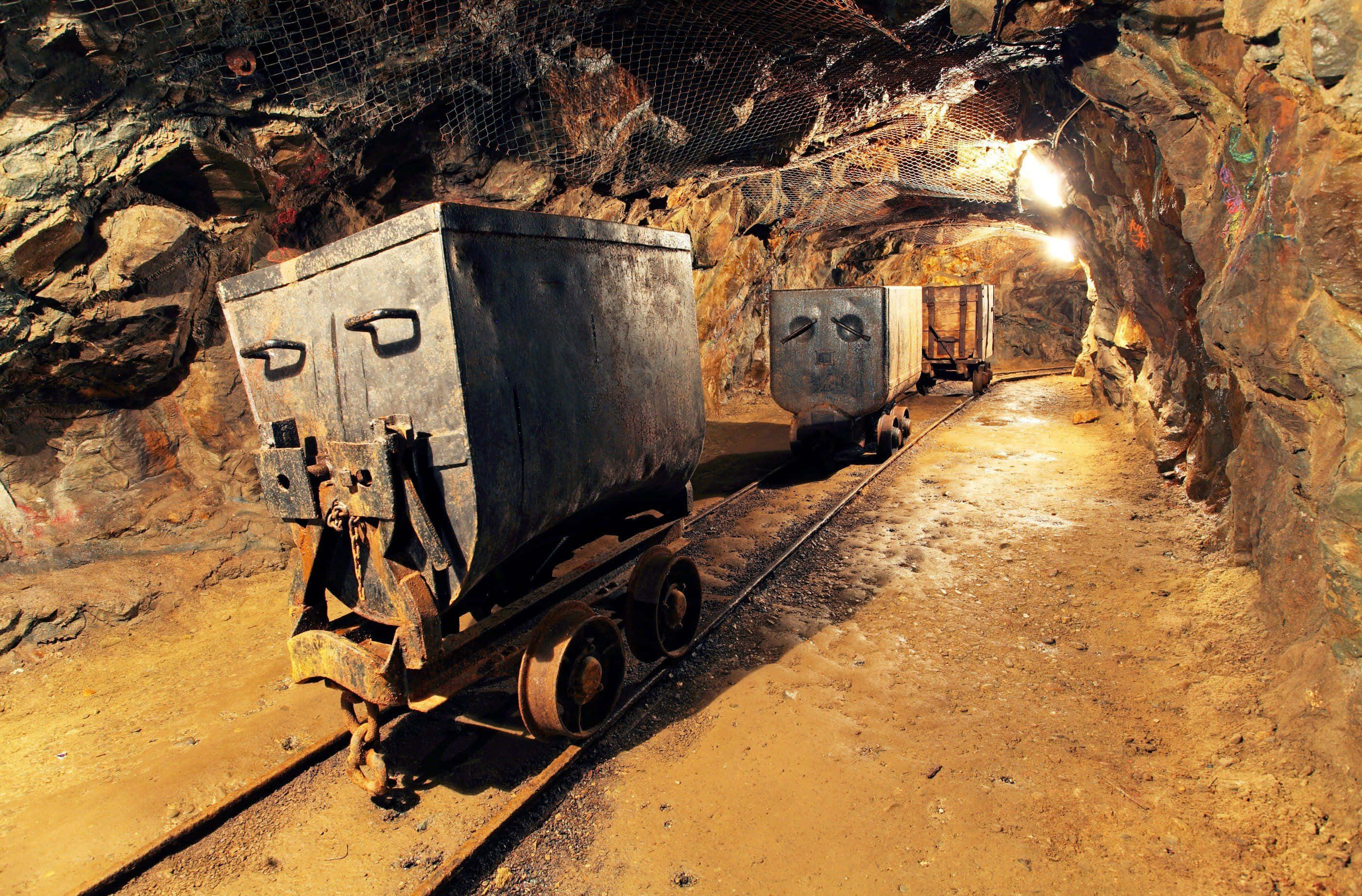 Mining 桌布 壁紙 — 生鏽的礦車停在昏暗地下隧道的軌道上，四周是粗糙的岩壁和安全網。