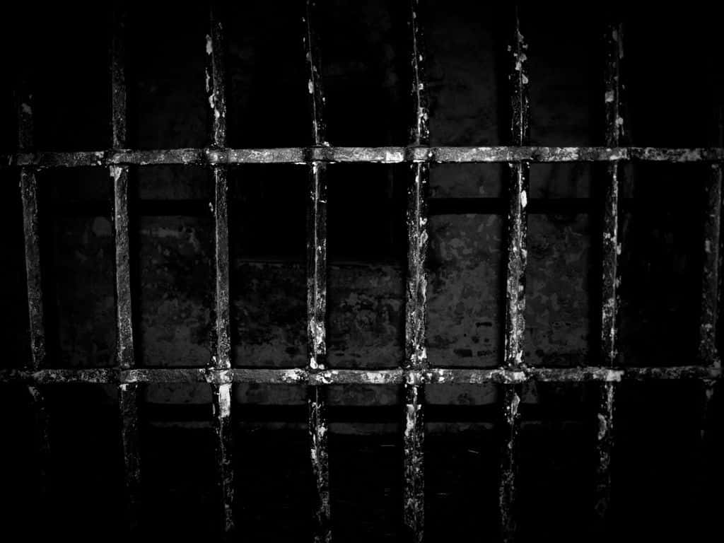 Prison Cell 桌布 壁紙 — 生鏽的金屬監獄鐵欄以單色調在深色背景下營造出嚴峻壓迫的網格。