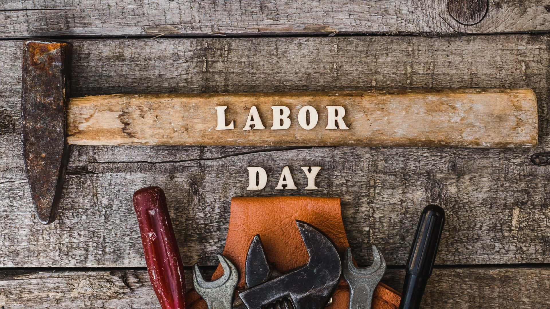 勞動節 桌布 壁紙 — 生鏽的錘子和扳手放在風化的木頭上，上面有 'LABOR DAY' 字樣。