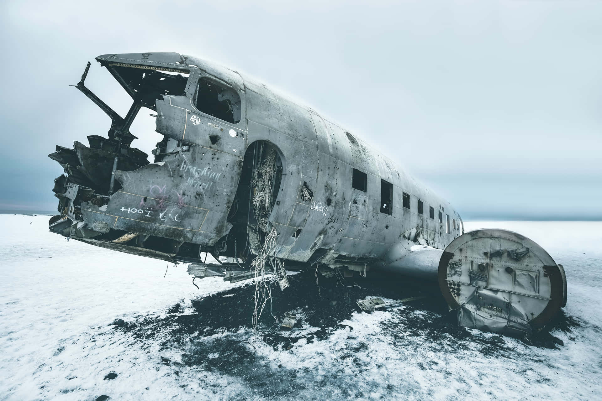  壁紙 — 生鏽的飛機機身被遺棄在廣闊的雪地上，天空灰濛濛。