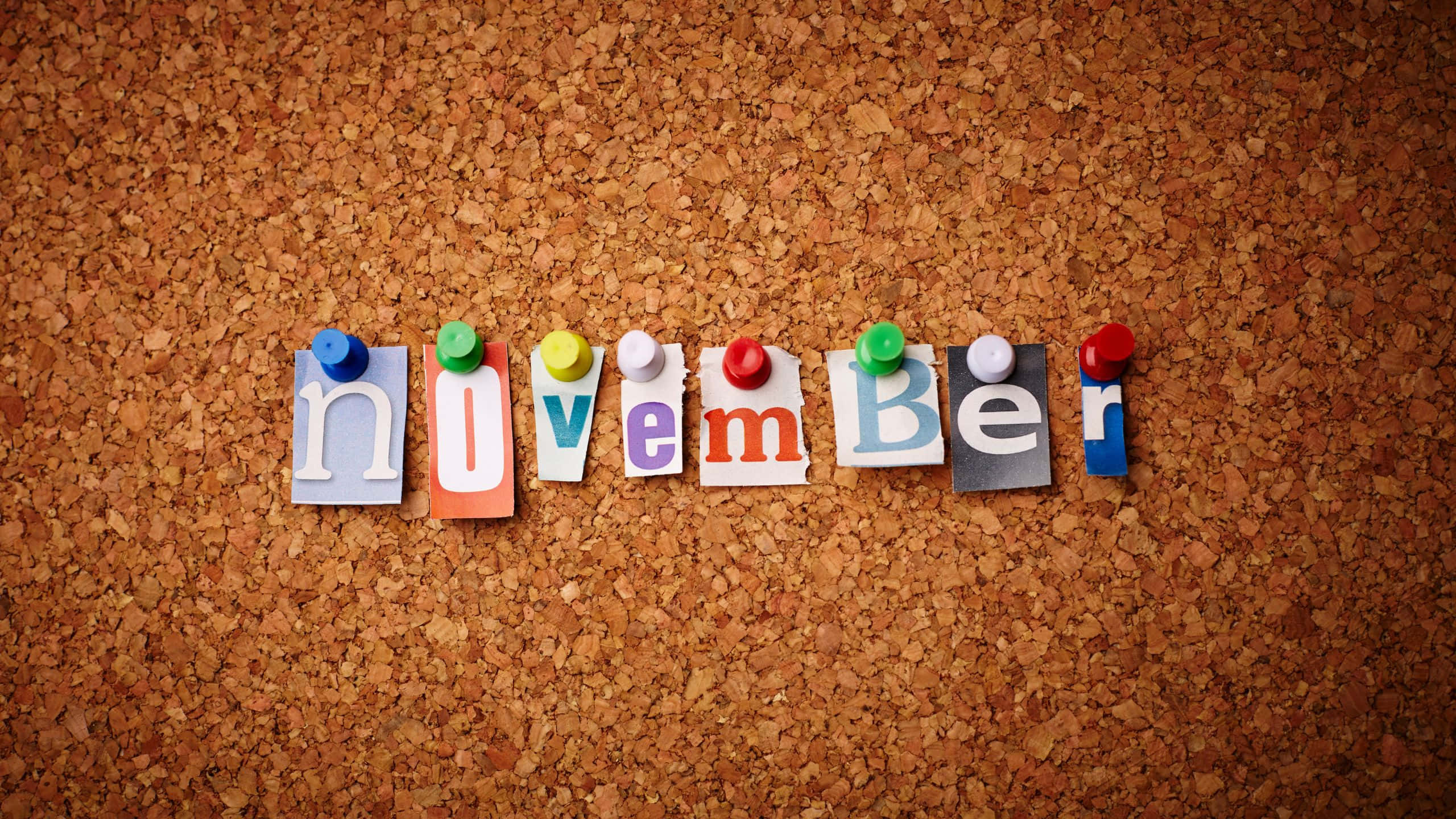 November Desktop 桌布 壁紙 — 用彩色紙字母拼成的單詞november，固定在帶有紋理的軟木板上。