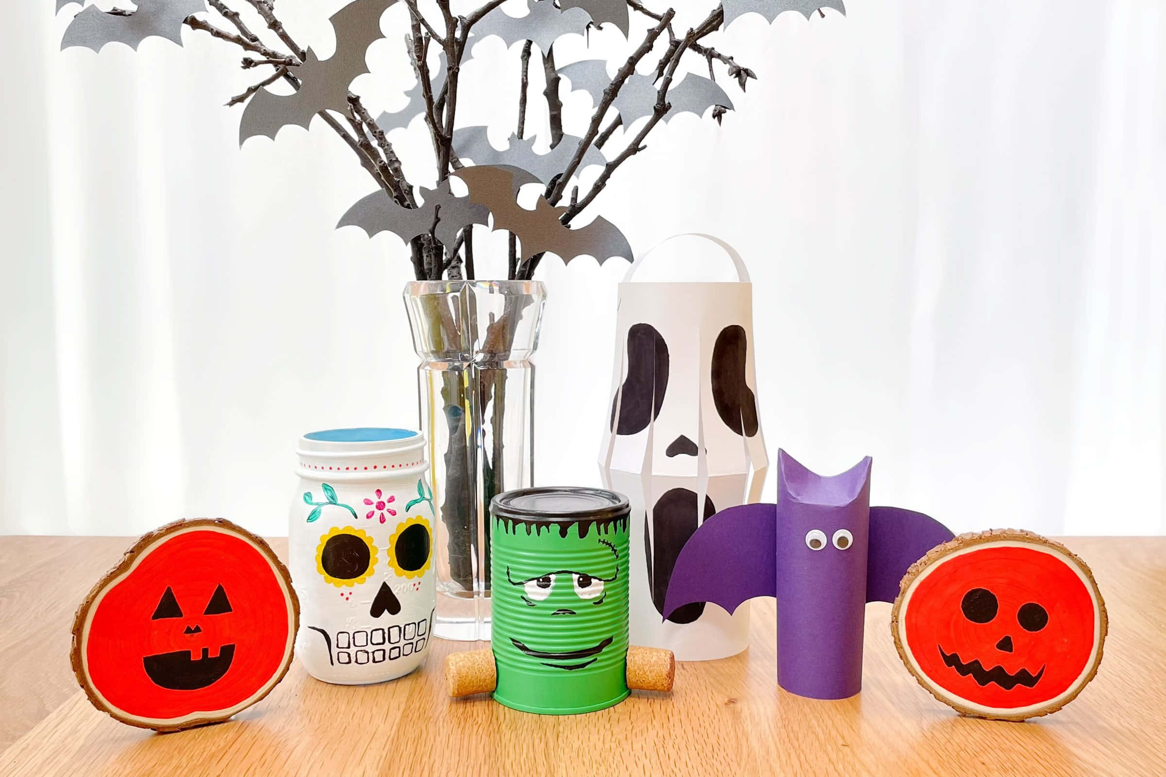 Halloween Props 桌布 壁紙 — 用木片、罐頭和紙管製作的萬聖節手工藝品，排列在木桌上，後方的花瓶中有蝙蝠剪紙。