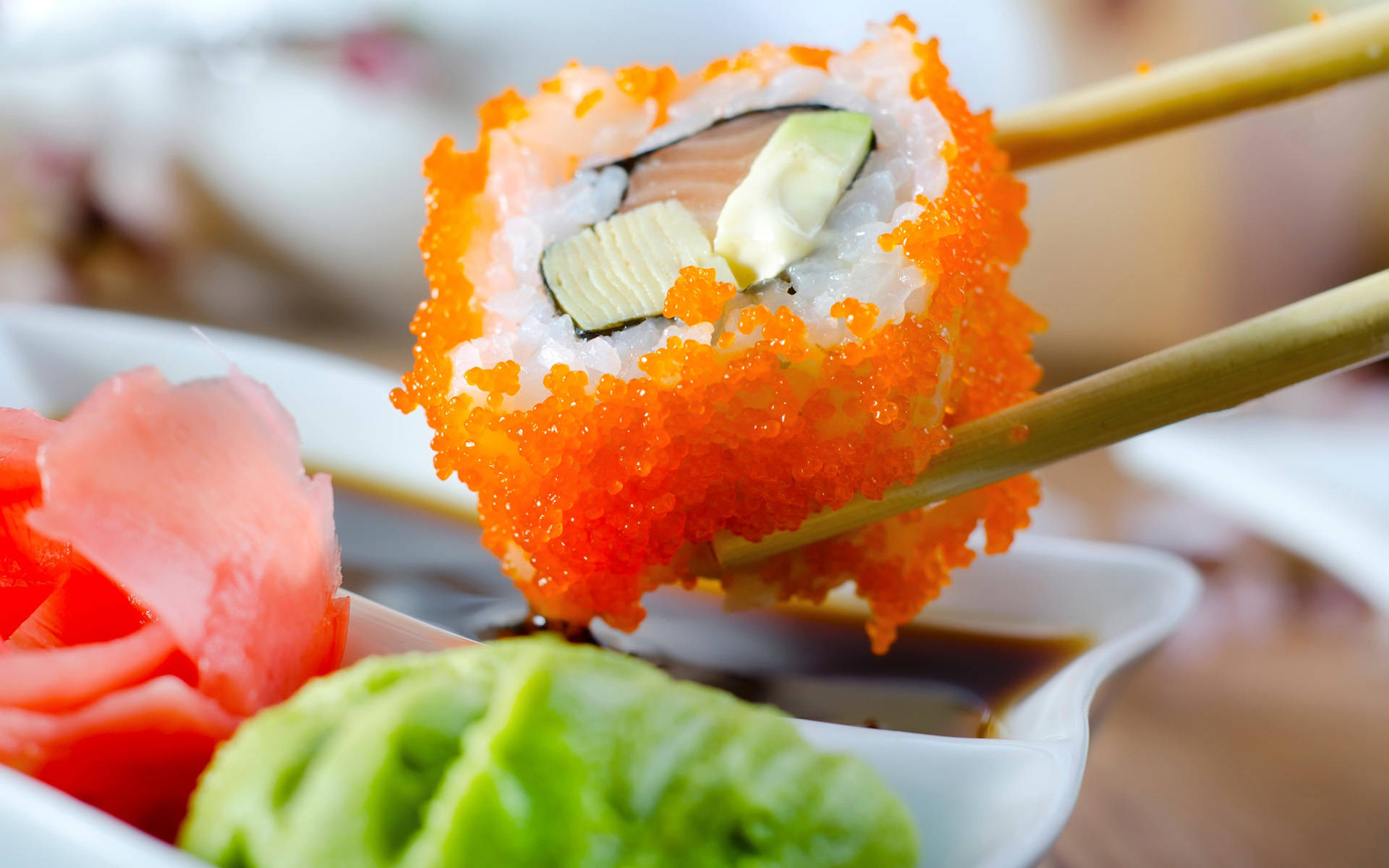 Sushi 桌布 壁紙 — 用筷子夾住飛魚籽壽司卷的特寫，置於醬油、芥末和生薑之上。