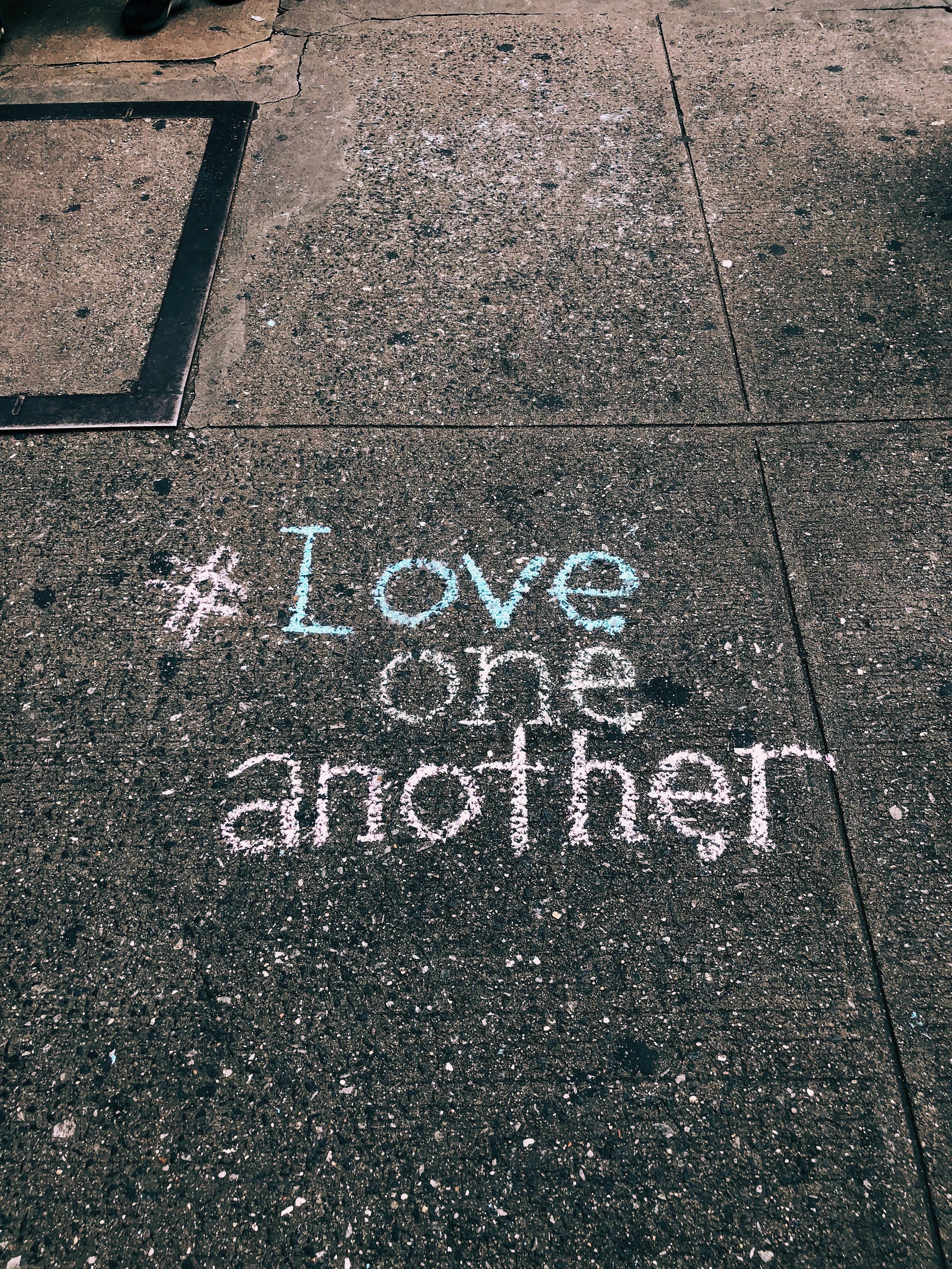 勵志動圖 桌布 壁紙 — 用粉筆寫在裂開的混凝土人行道上的訊息 love one another，附有 hashtag 符號。
