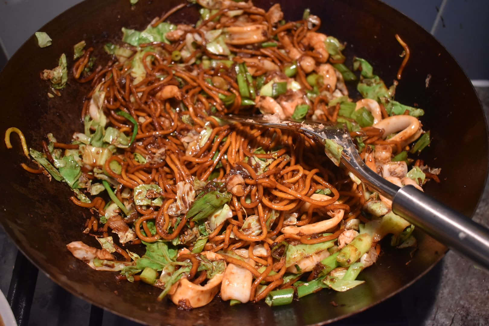 Delicious Food 桌布 壁紙 — 用金屬鍋鏟在鍋中翻炒的鐵板炒麵，搭配魷魚和綠色蔬菜。