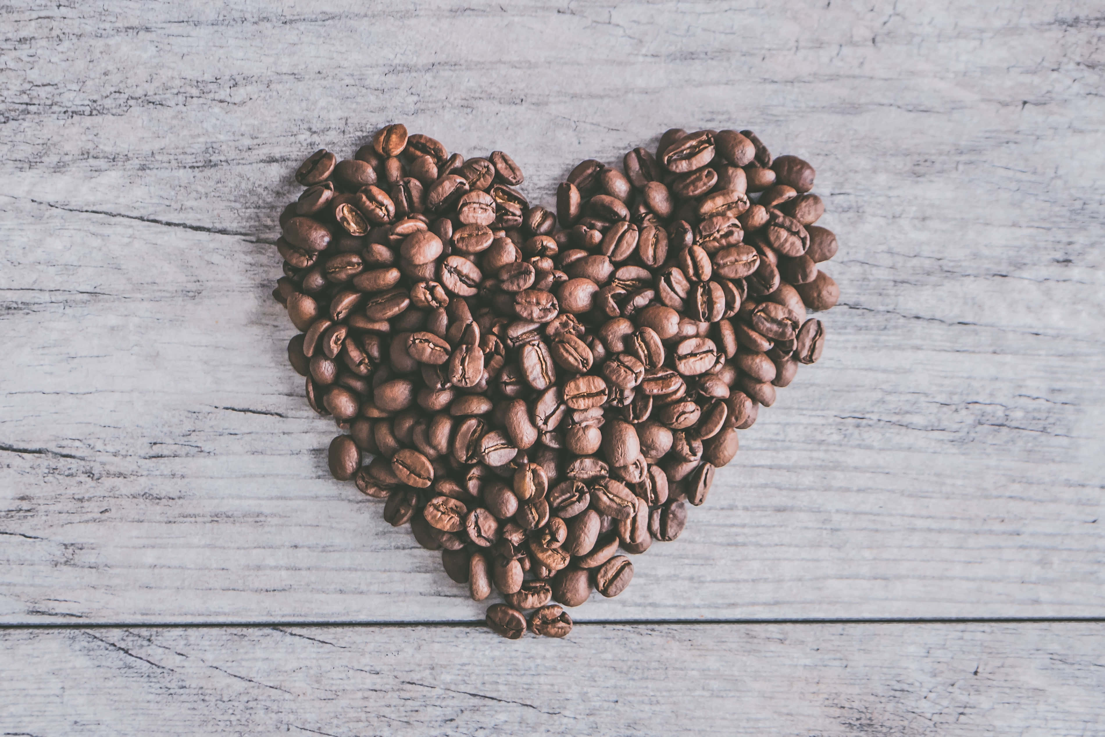 Coffee Beans 桌布 壁紙 — 由烘焙咖啡豆形成的心形圖案，放置在經風化的白色木質表面上。